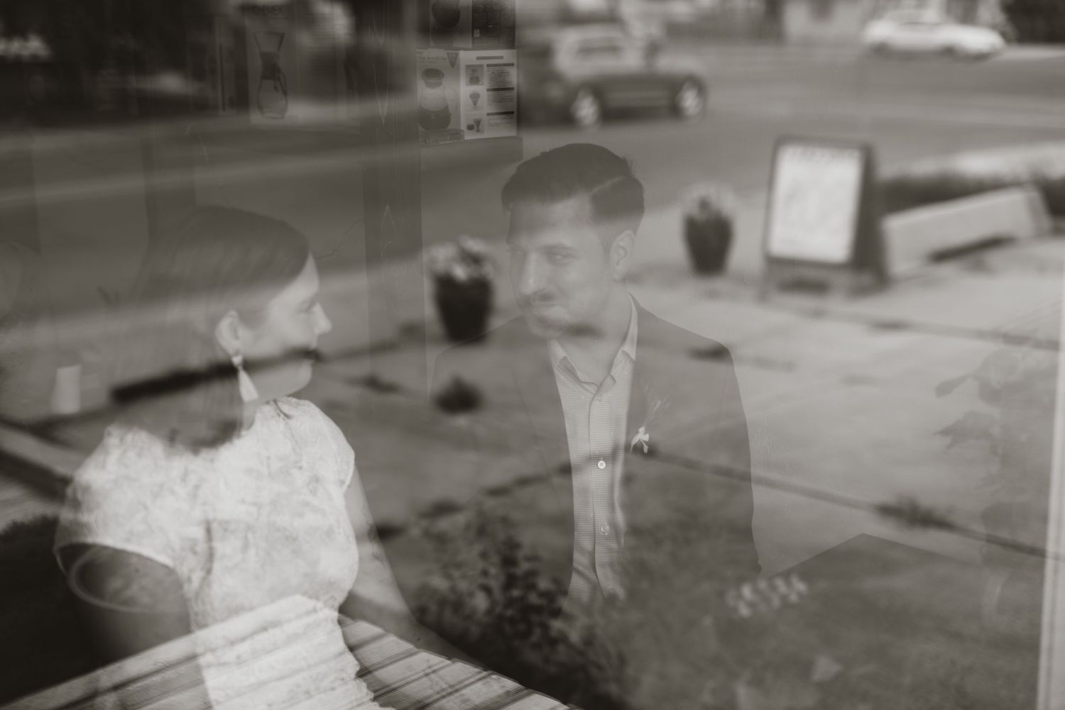 Black and white window reflection of eloping couple in Calgary. Artsy, emotional wedding portrait with city street backdrop.