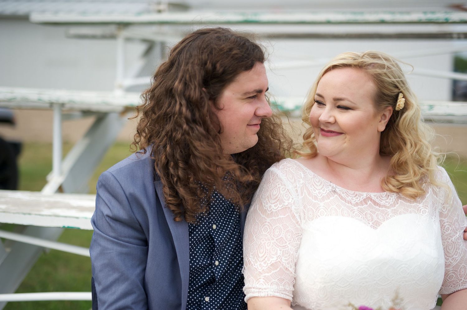 Wedding couple sitting closely on metal bleachers, gazing at each other and smiling, with casual and heartfelt energy.