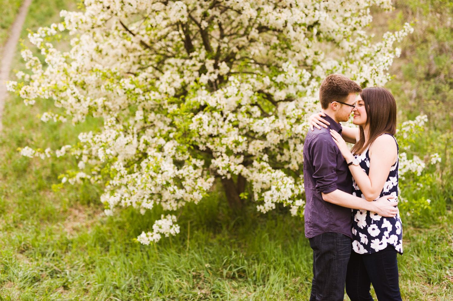 Couple standing closely in front of a blooming tree, faces nearly touching, in soft golden light.
