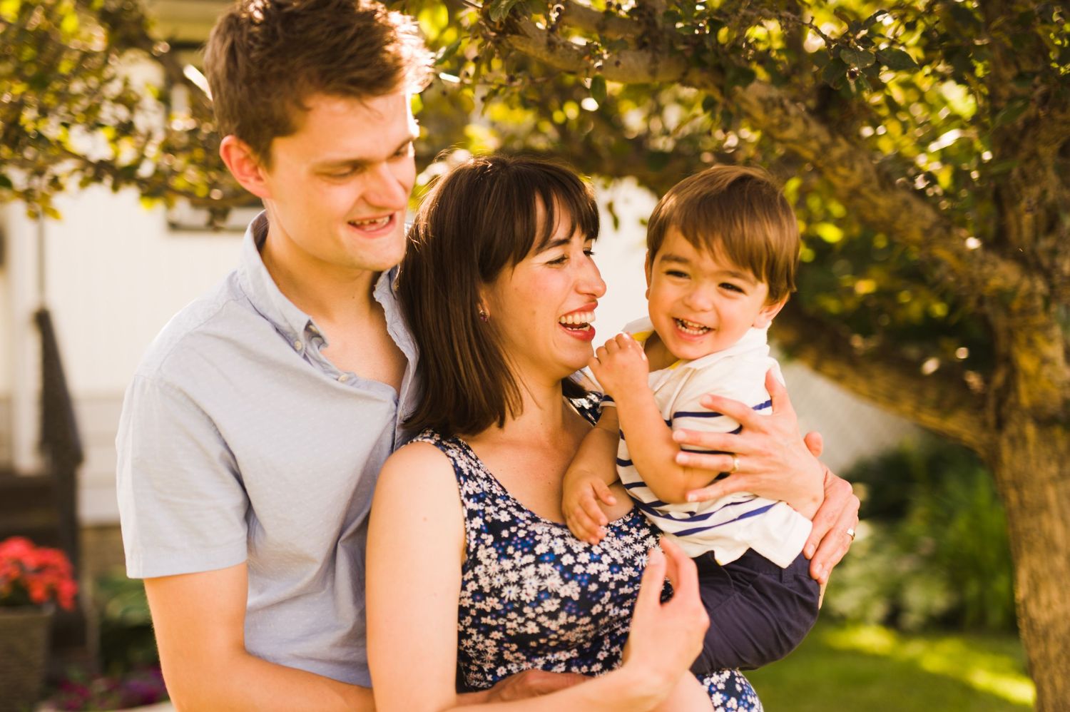 \Parents holding their joyful toddler between them, sharing a warm laugh together outside.
