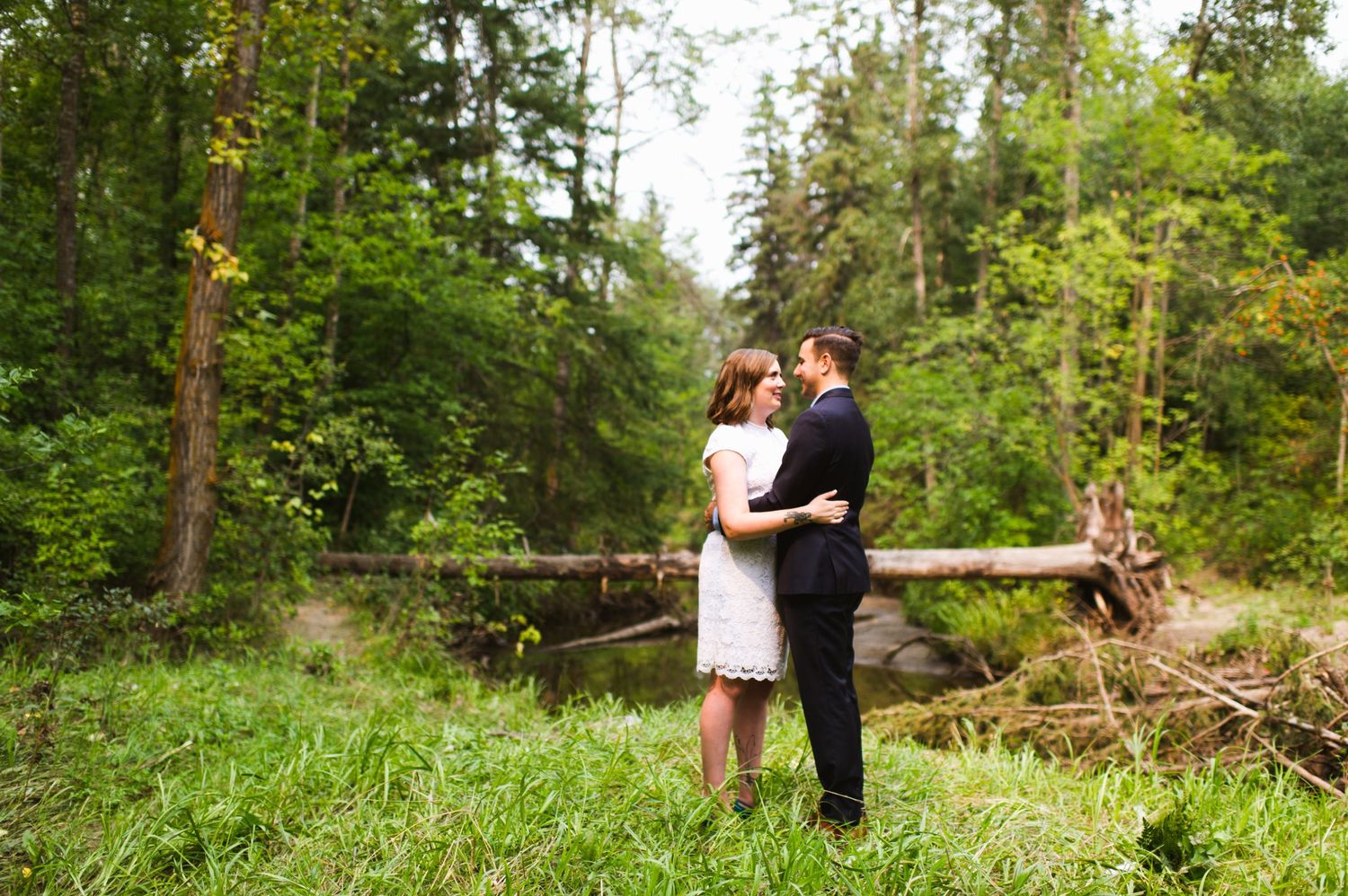 Quiet embrace in lush green forest clearing. Romantic outdoor elopement photography in Alberta’s river valley.