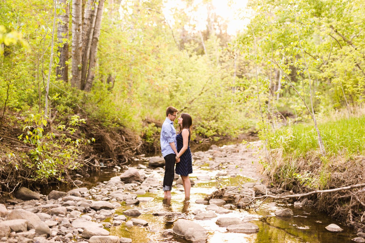 Couple holding hands and sharing a quiet moment while standing in a sun-dappled creek.