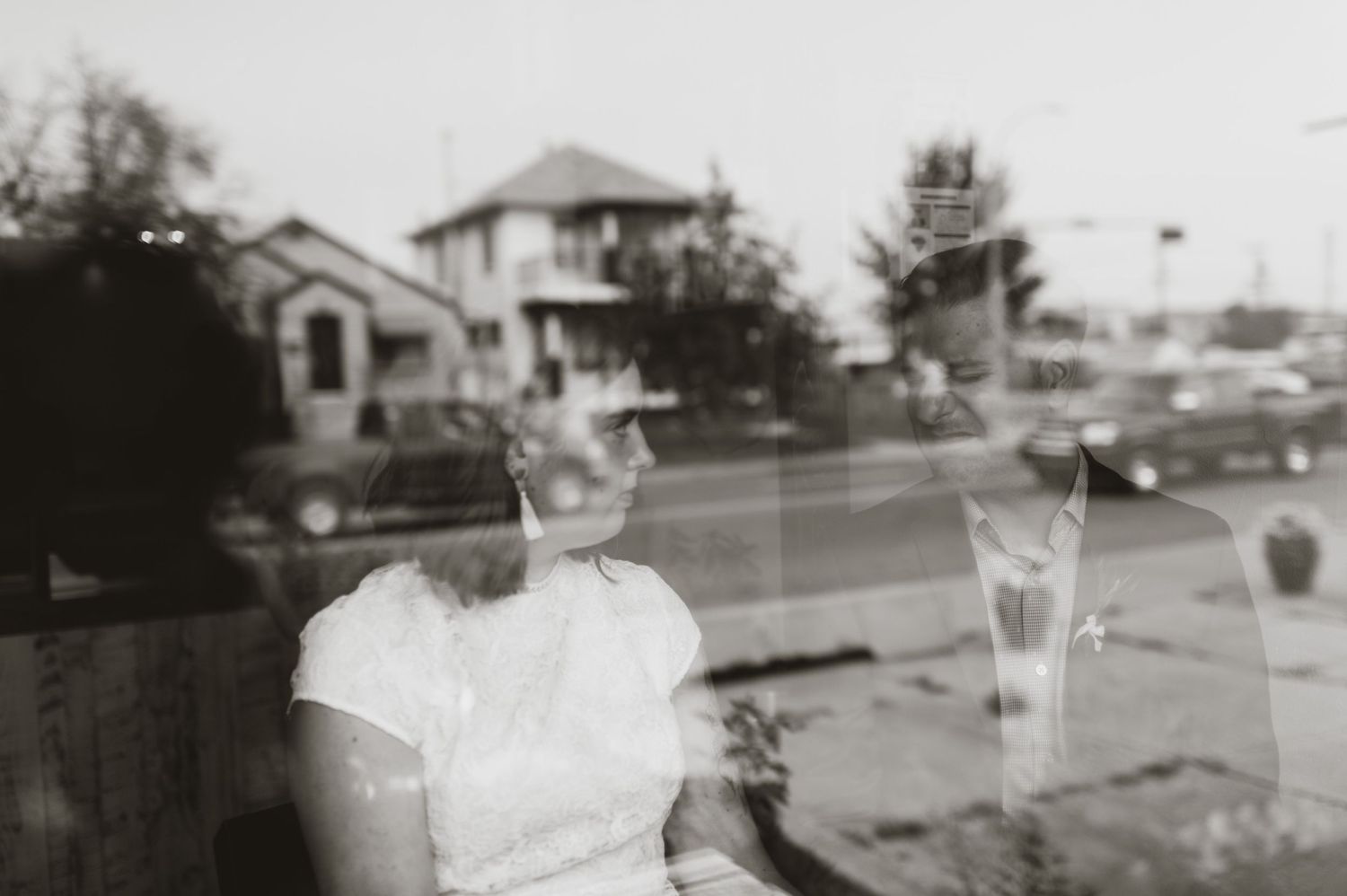 Bride in short white dress reflected in window beside groom. Calgary street-style elopement with vintage charm.