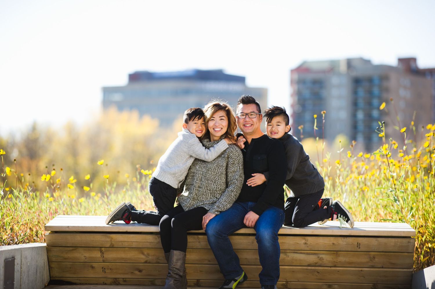 Family of four hugging and smiling on a sunny rooftop garden with city buildings in the background.