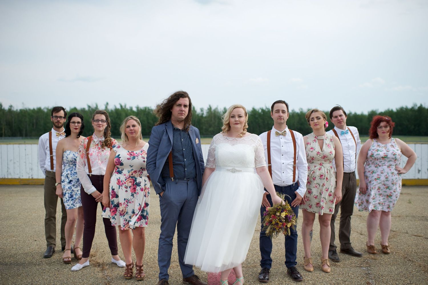 Bride and groom walking confidently with their wedding party behind them, posed in and outdoor rink in coordinated floral outfits.