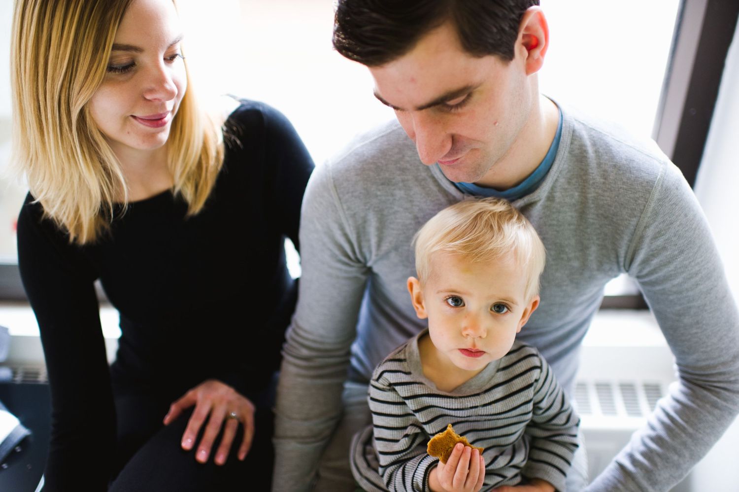 Family cuddles with toddler on floor by window. Cozy in-home Calgary session with bright, honest storytelling.