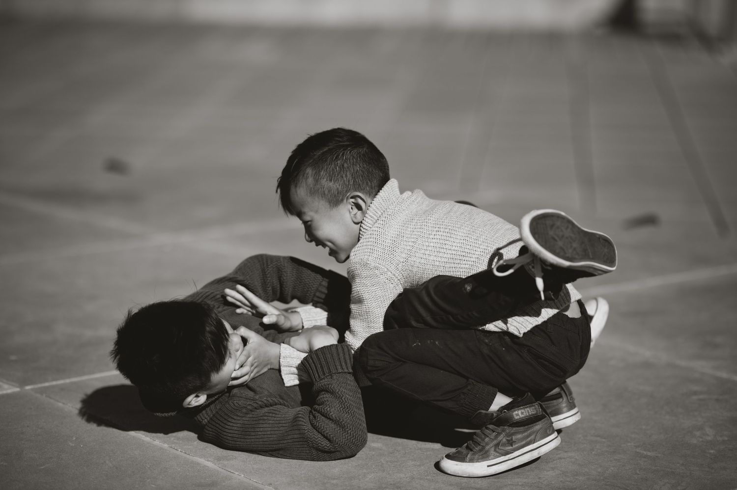 Black and white photo of boys wrestling on the ground, one pinning the other while they both smile.