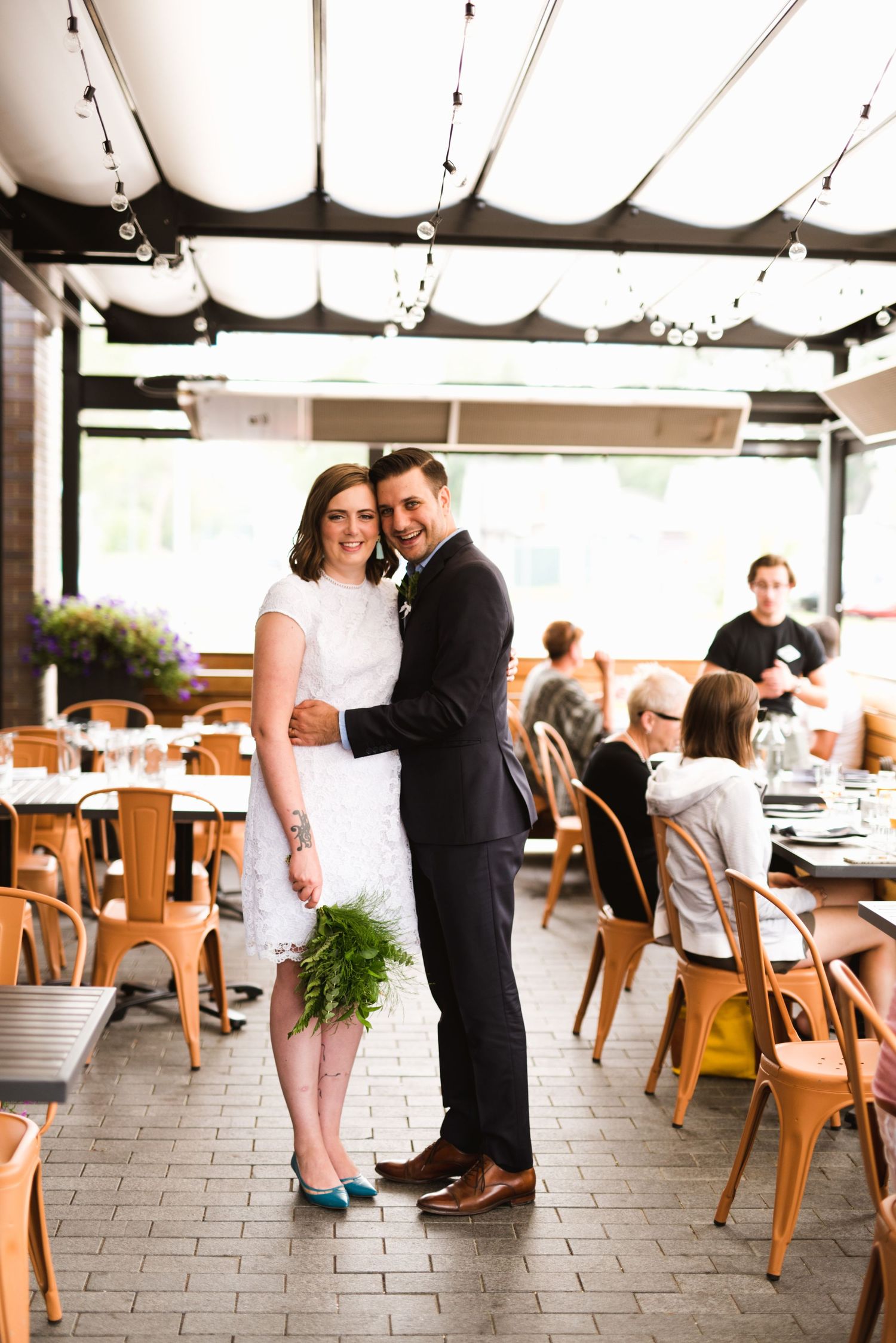 Couple hugs at brewery wedding. Indoor elopement reception with casual seating and modern lighting.