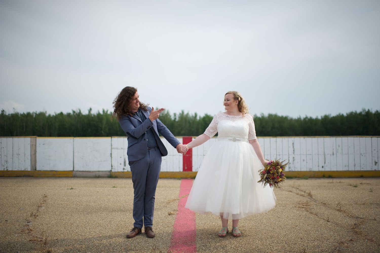 Bride and groom holding hands and smiling at each other mid-step on an outdoor rink, walking along the red center line.