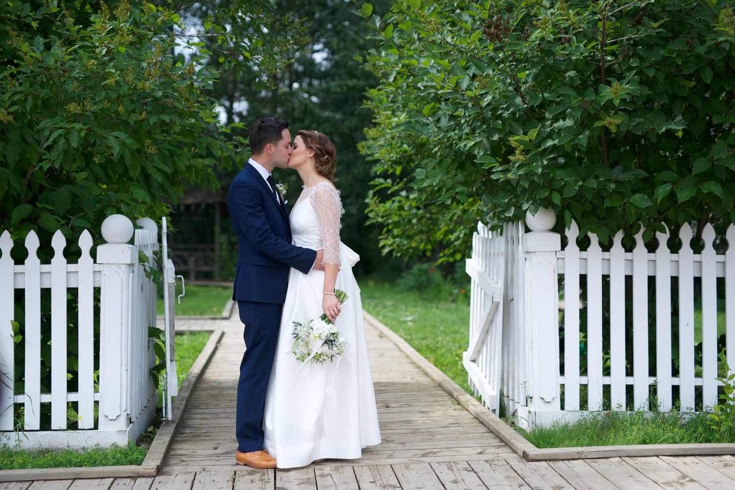 Couple kisses by a white gate framed with greenery. A garden moment that feels like the last page of a love story.