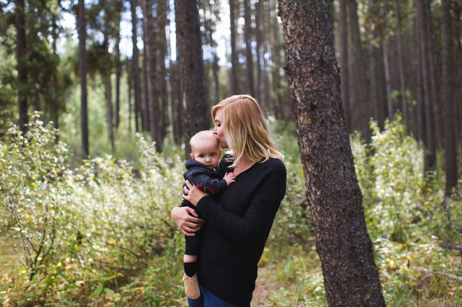 Mom cradles toddler in forest light. Jasper family photo session with warm, candid moments.