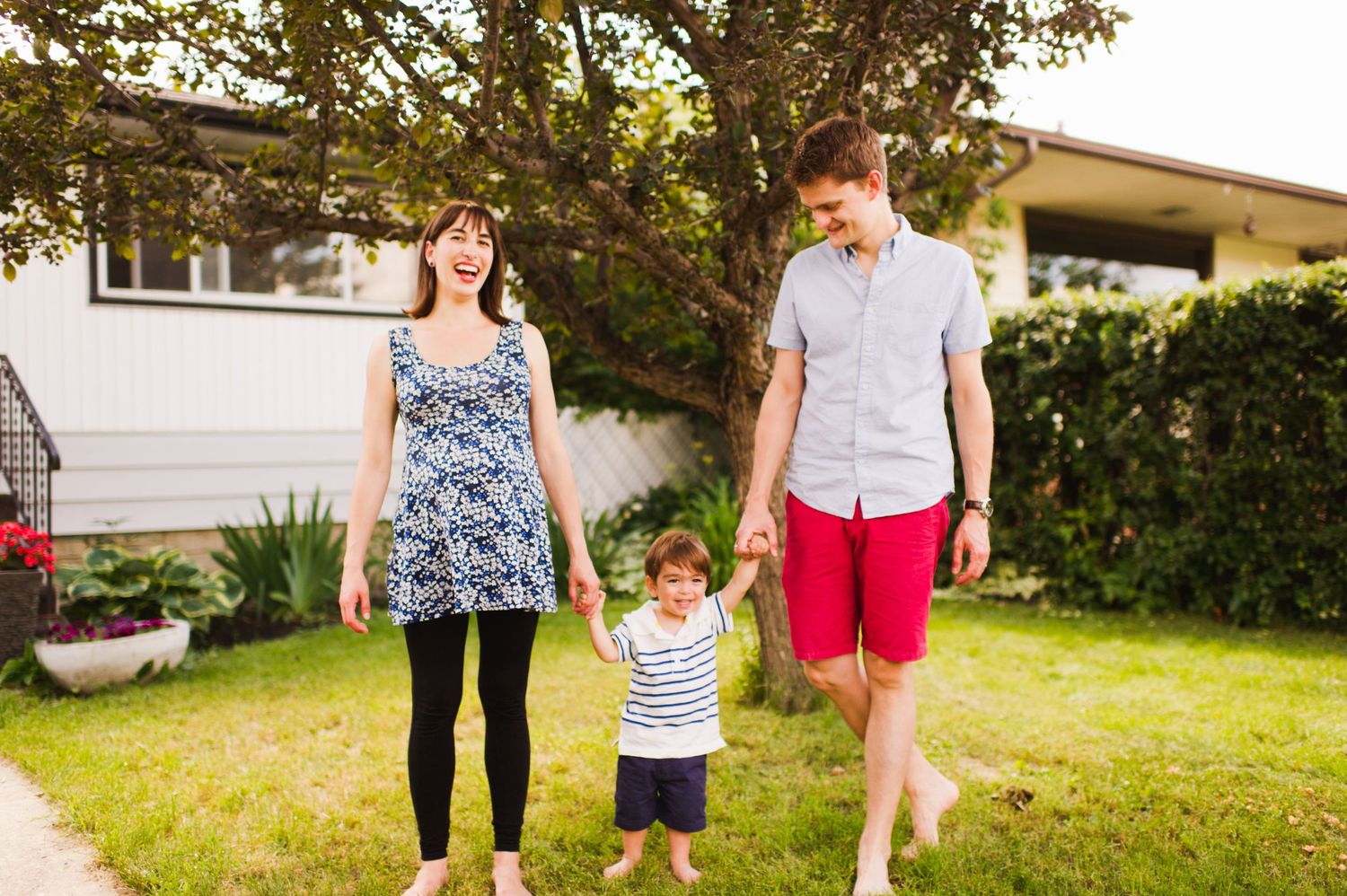 Parents holding their joyful toddler between them, sharing a warm laugh together outside. Maternity photo