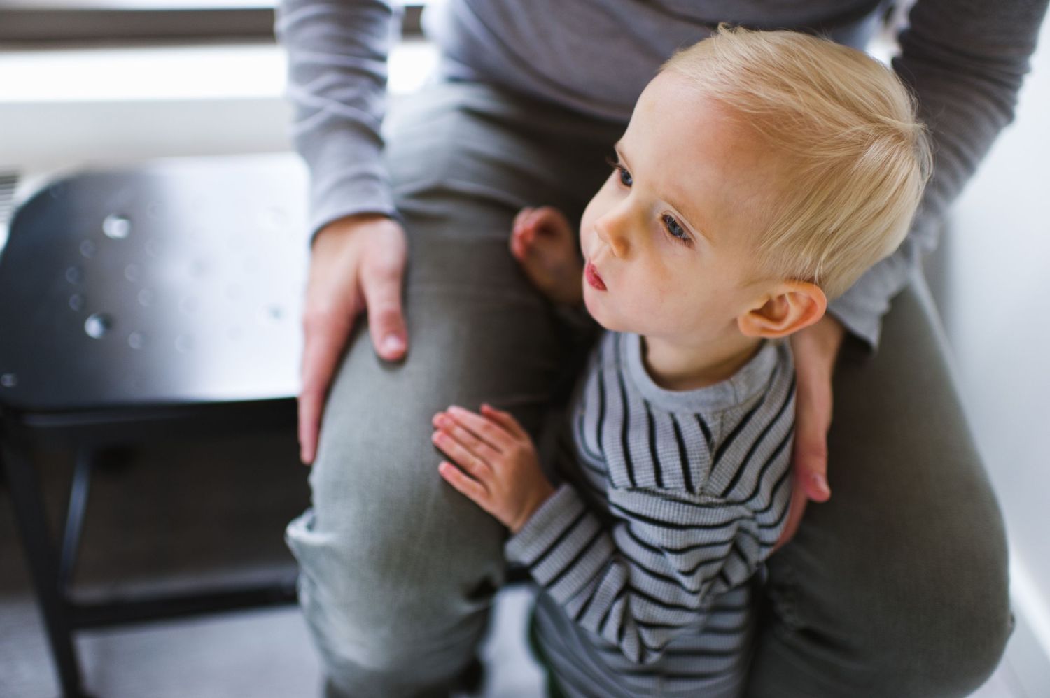 Close-up of toddler on parent’s lap at home. Candid indoor lifestyle session with natural light.