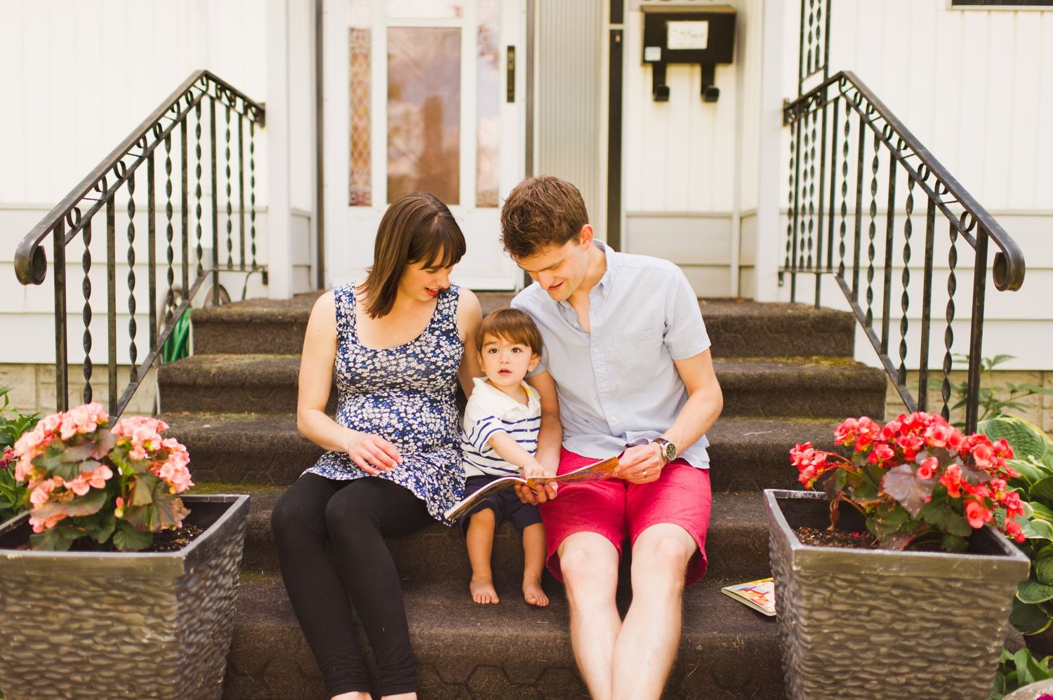 Family of three sitting on their front steps, looking at their toddler with love and warmth.