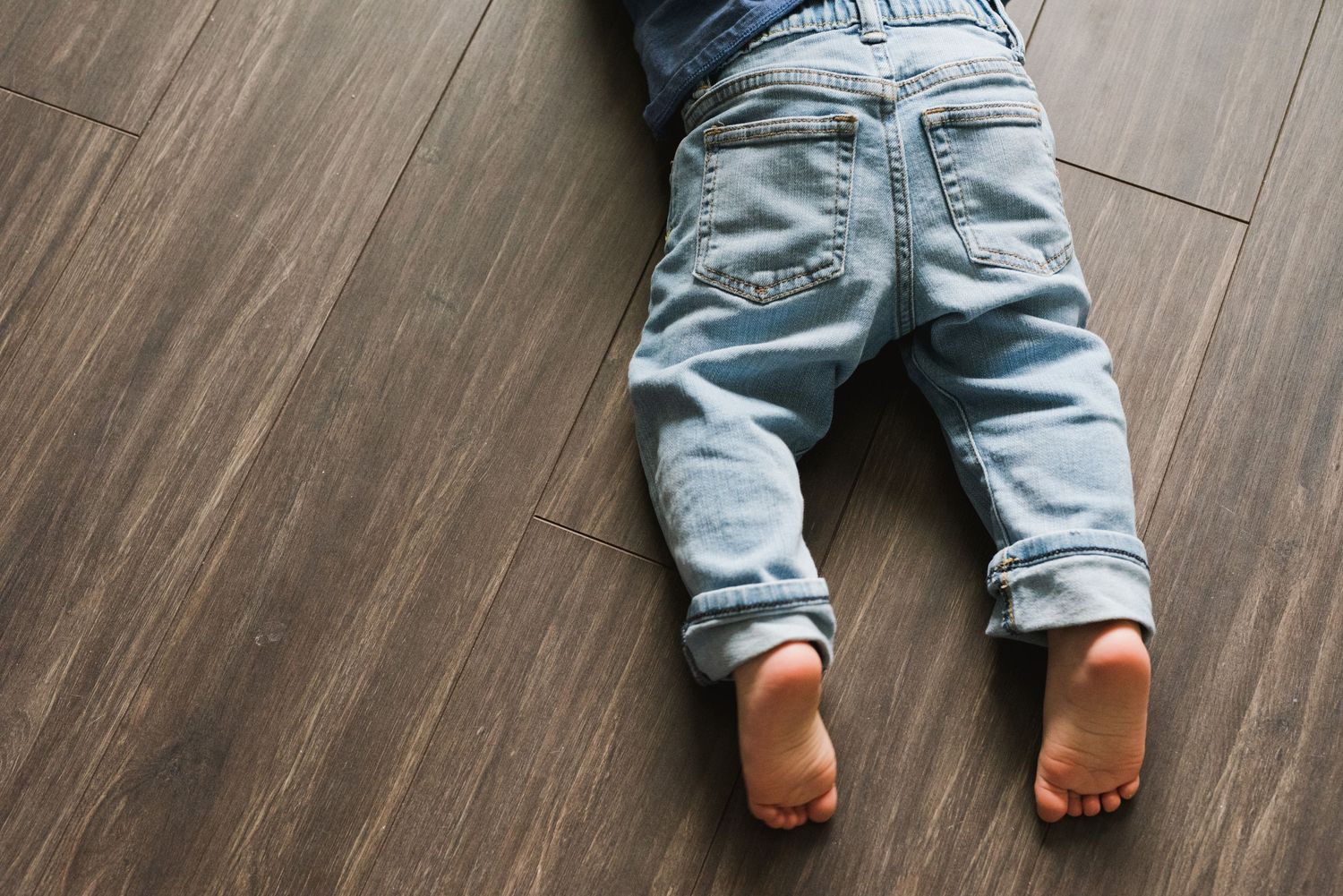 Toddler lying face down on a hardwood floor, legs stretched out in playful stillness.