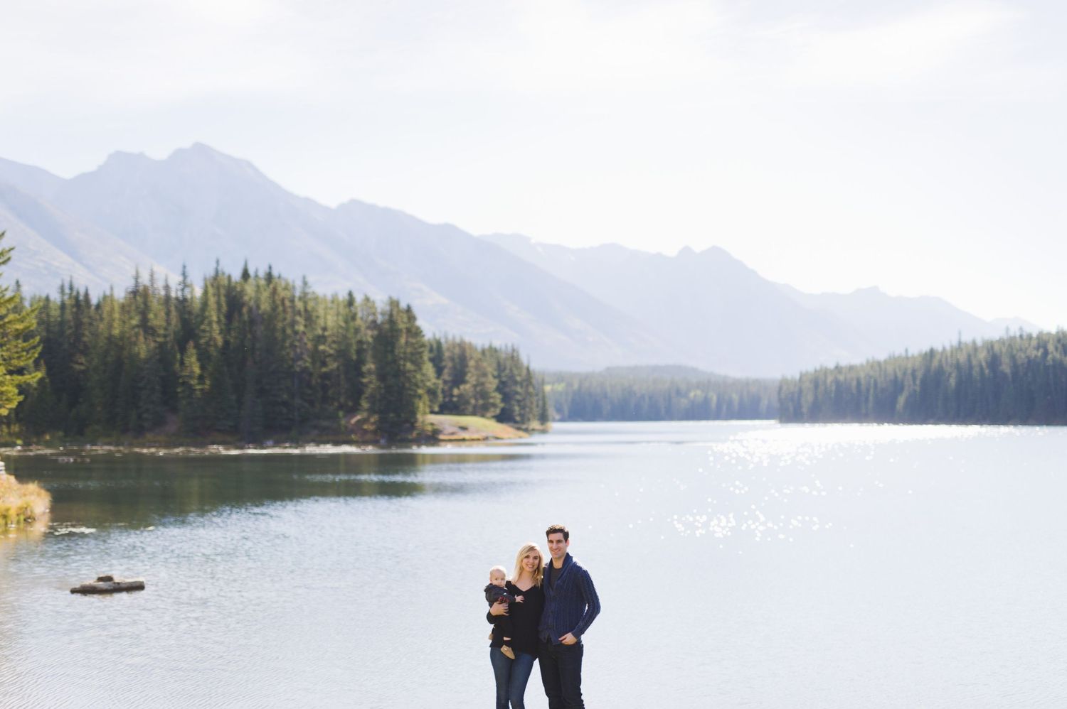 Couple embraces lakeside in Kananaskis with mountain views. Alberta outdoor session for families or couples.