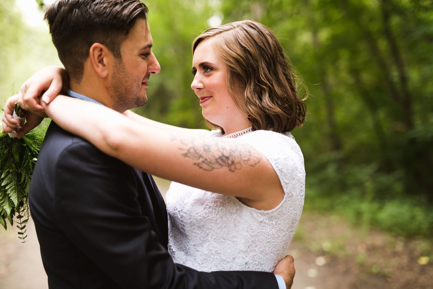 Bride and groom share a joyful embrace on a wooded trail. Summer forest elopement with natural connection.