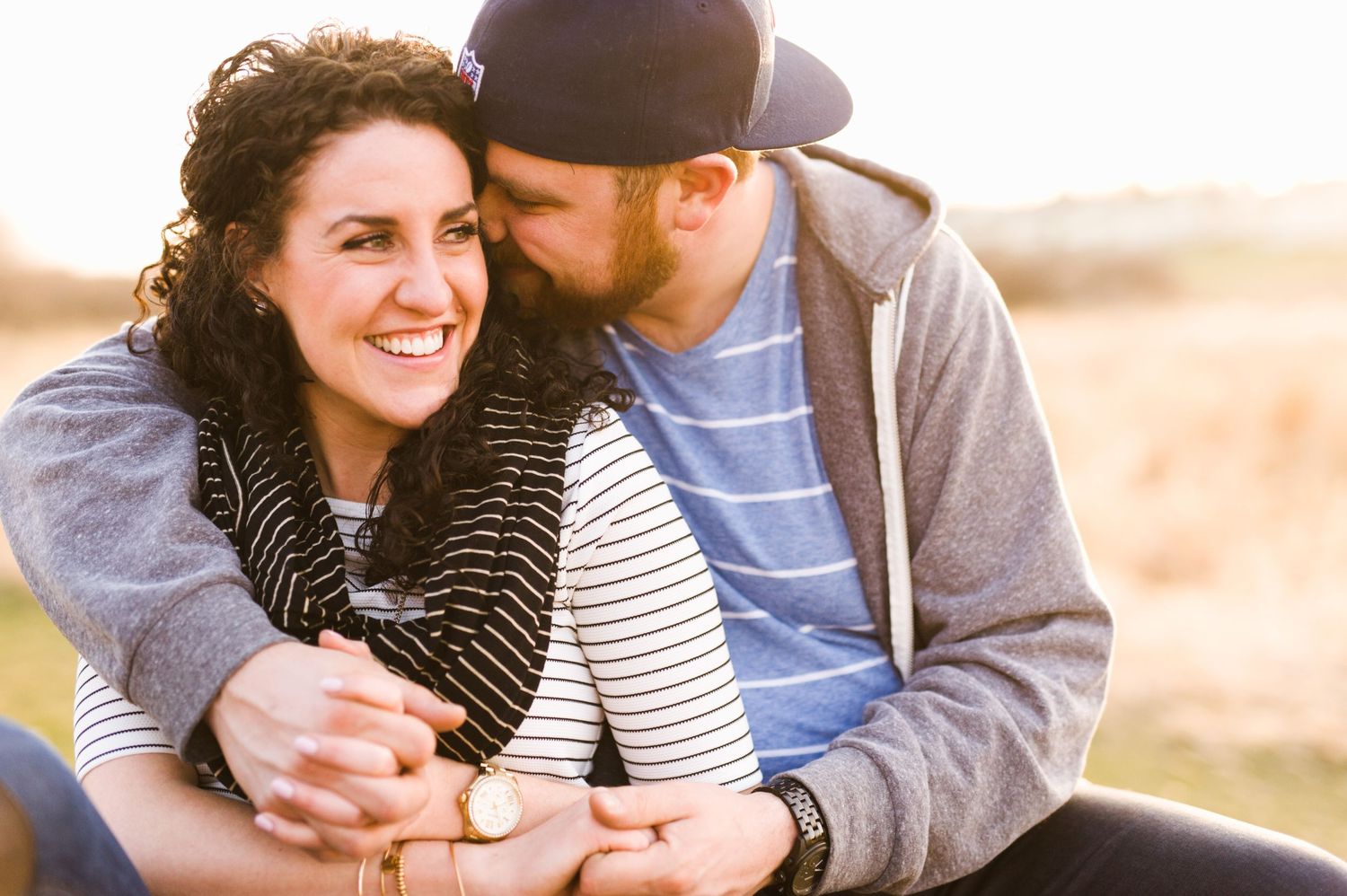 Couple cuddles during golden hour in Alberta field. Warm, relaxed engagement-style portrait full of connection.