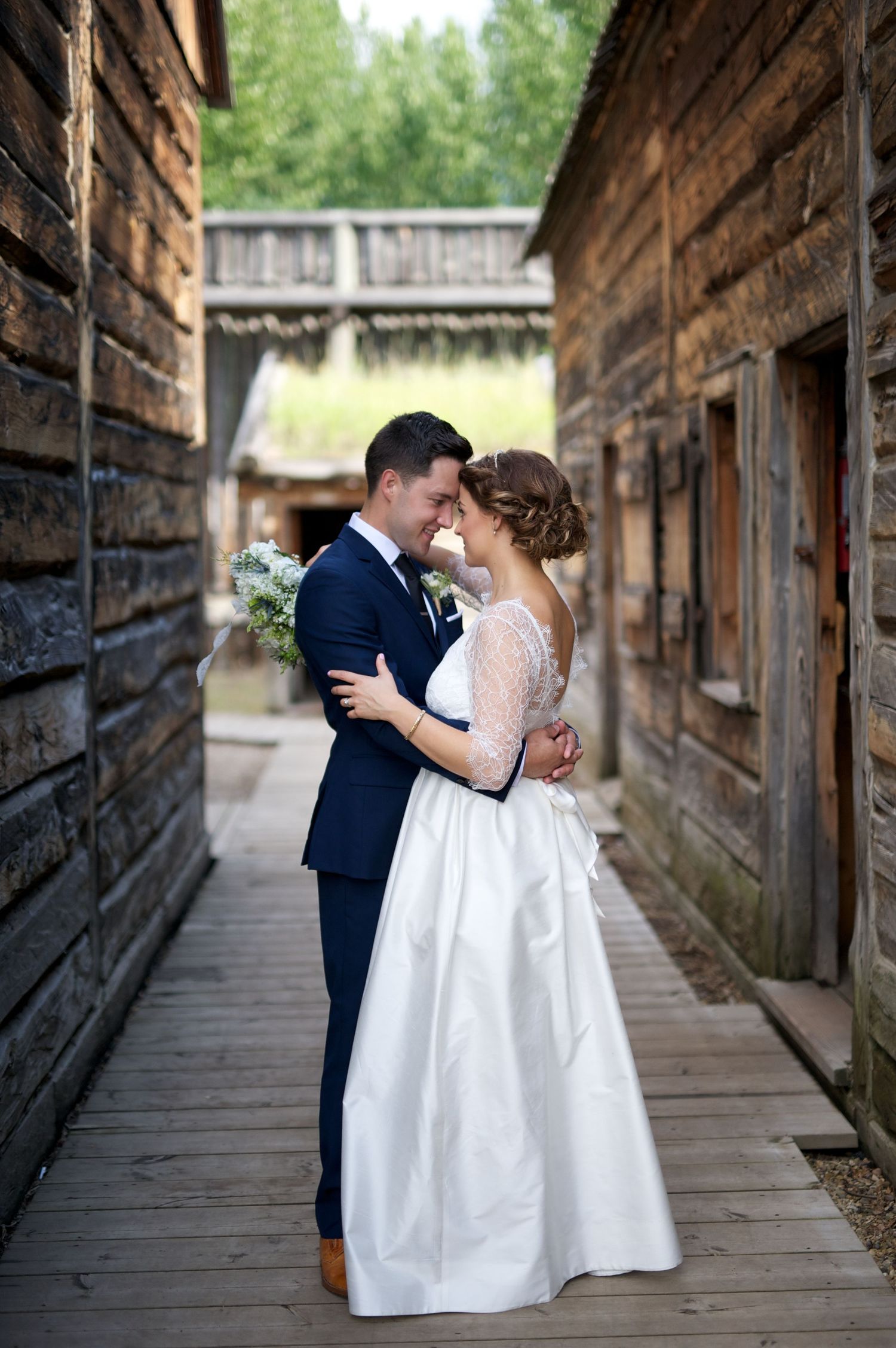 Bride and groom embracing closely in a narrow wooden alley, framed by vintage buildings.
