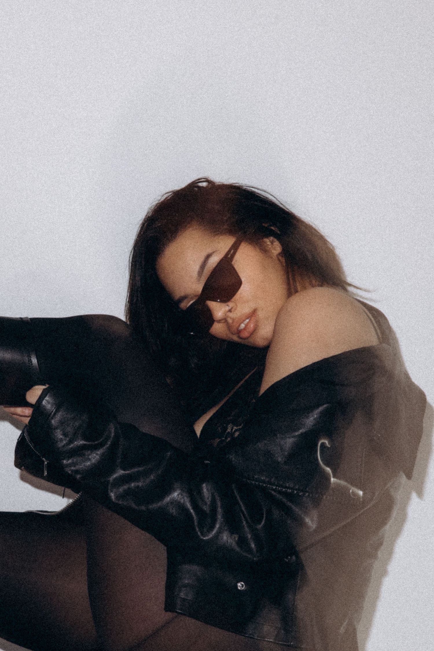 Artistic portrait shows model in leather jacket and sunglasses against white backdrop.