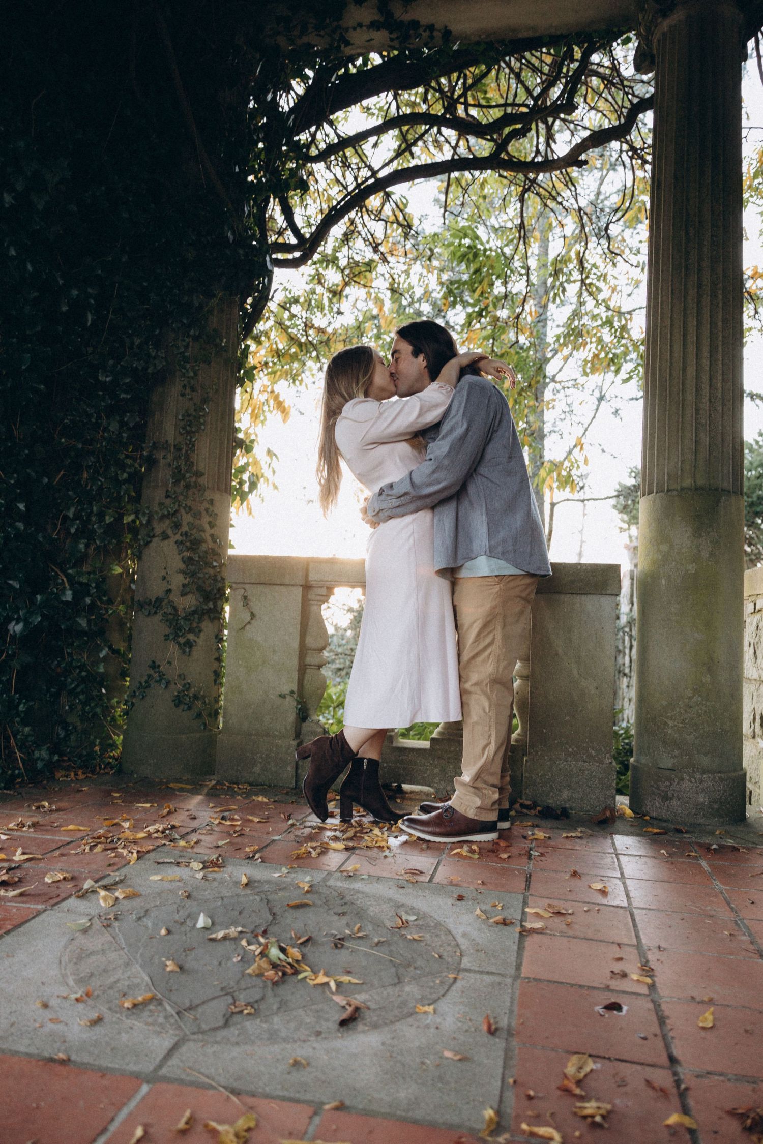 A romantic moment captured under an ivy-covered archway with autumn leaves scattered on the ground.
