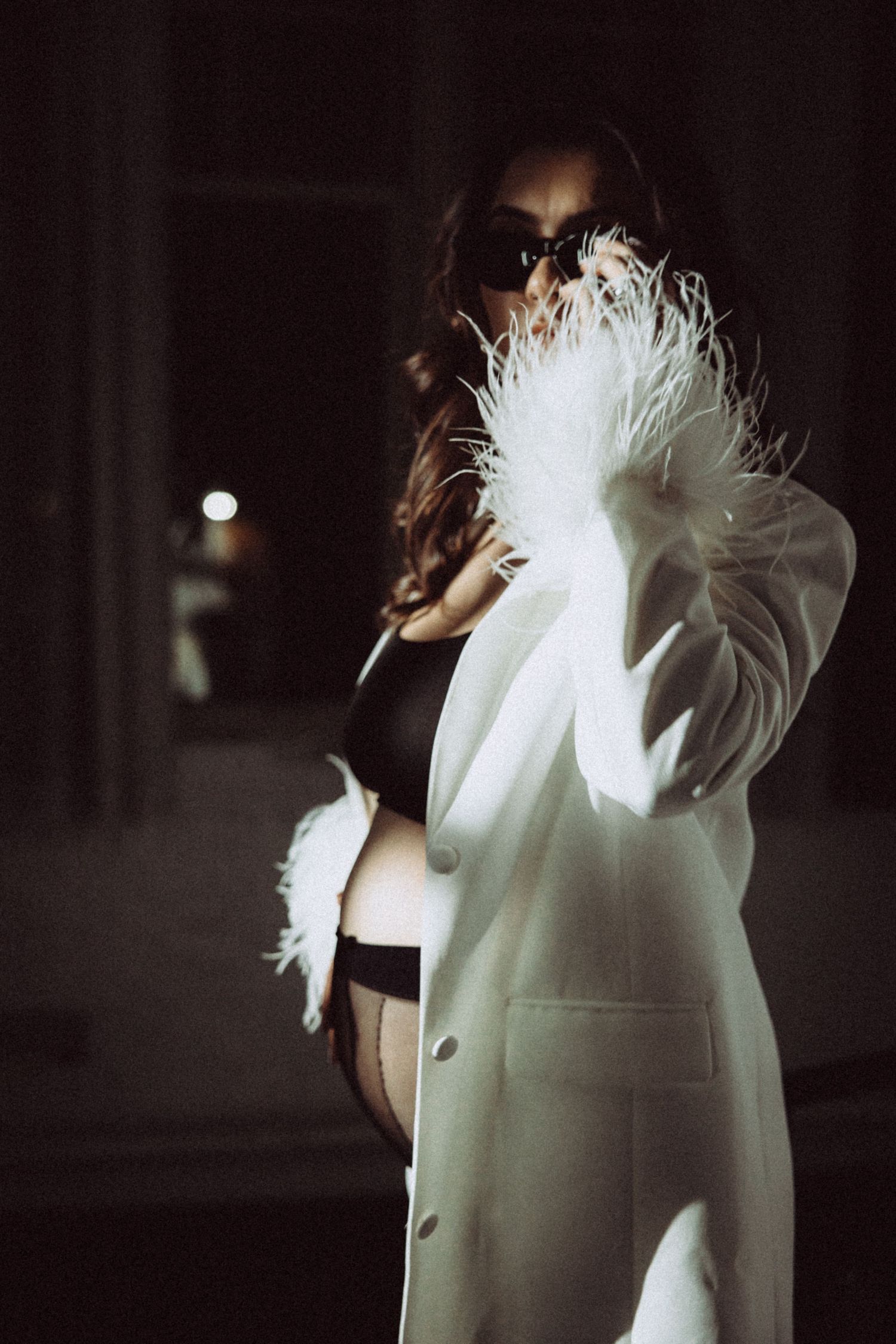 Moody fashion photo featuring white feather details and blazer against dark background.