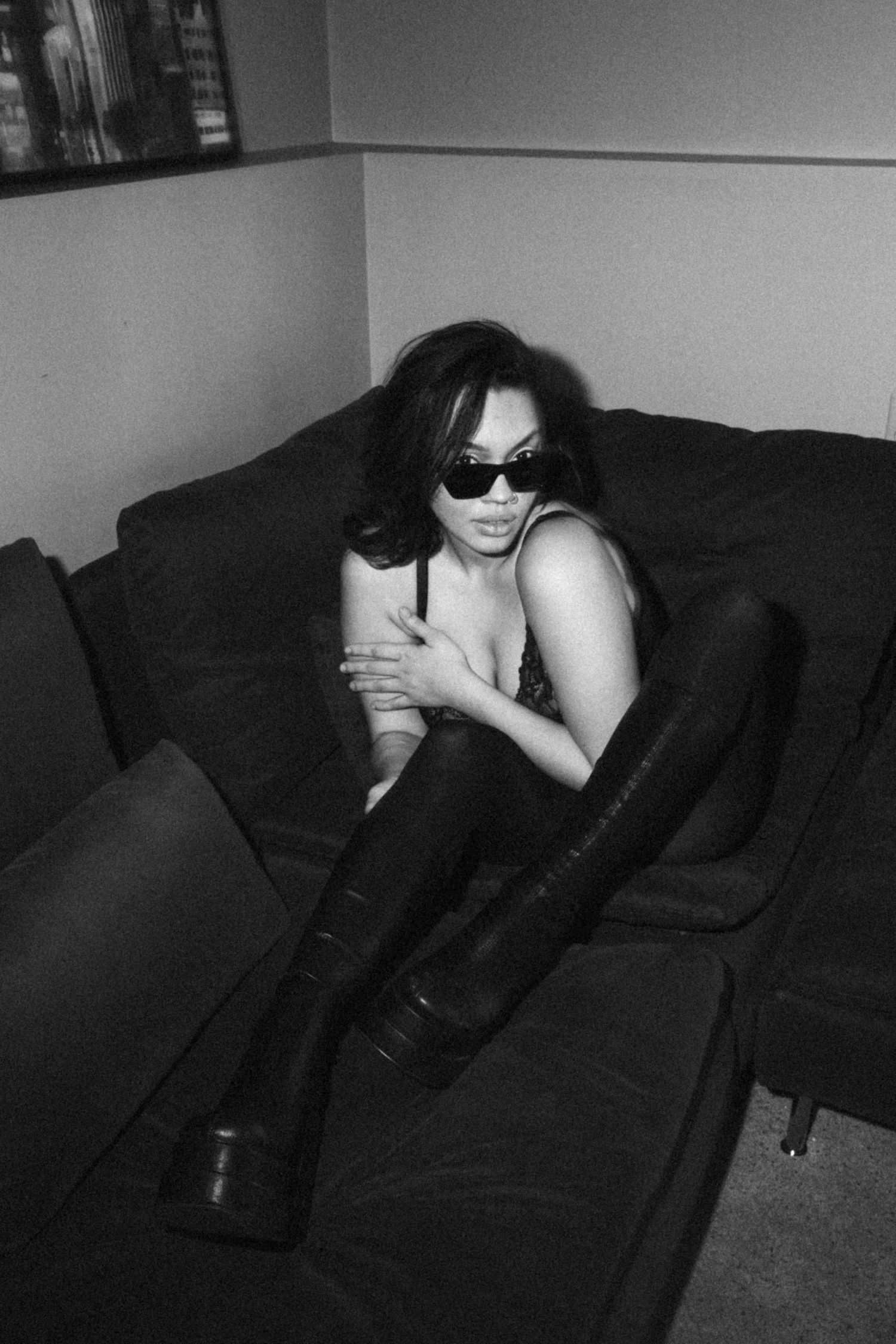 Monochrome photo of model lounging on dark couch wearing sunglasses and leather outfit.