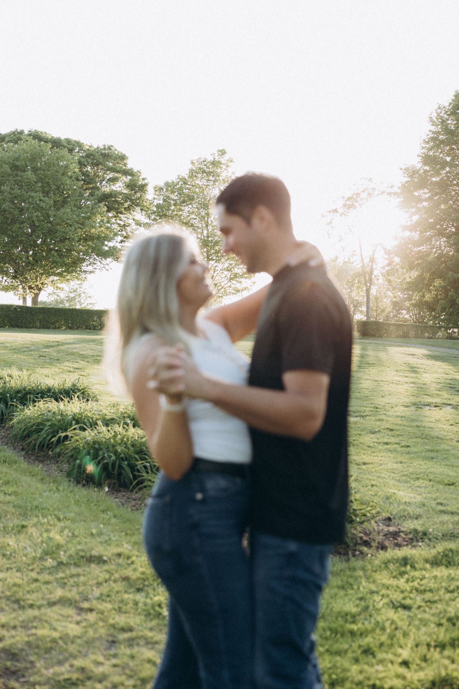 A couple dancing and embracing in a sunlit field with green grass and trees in the background.