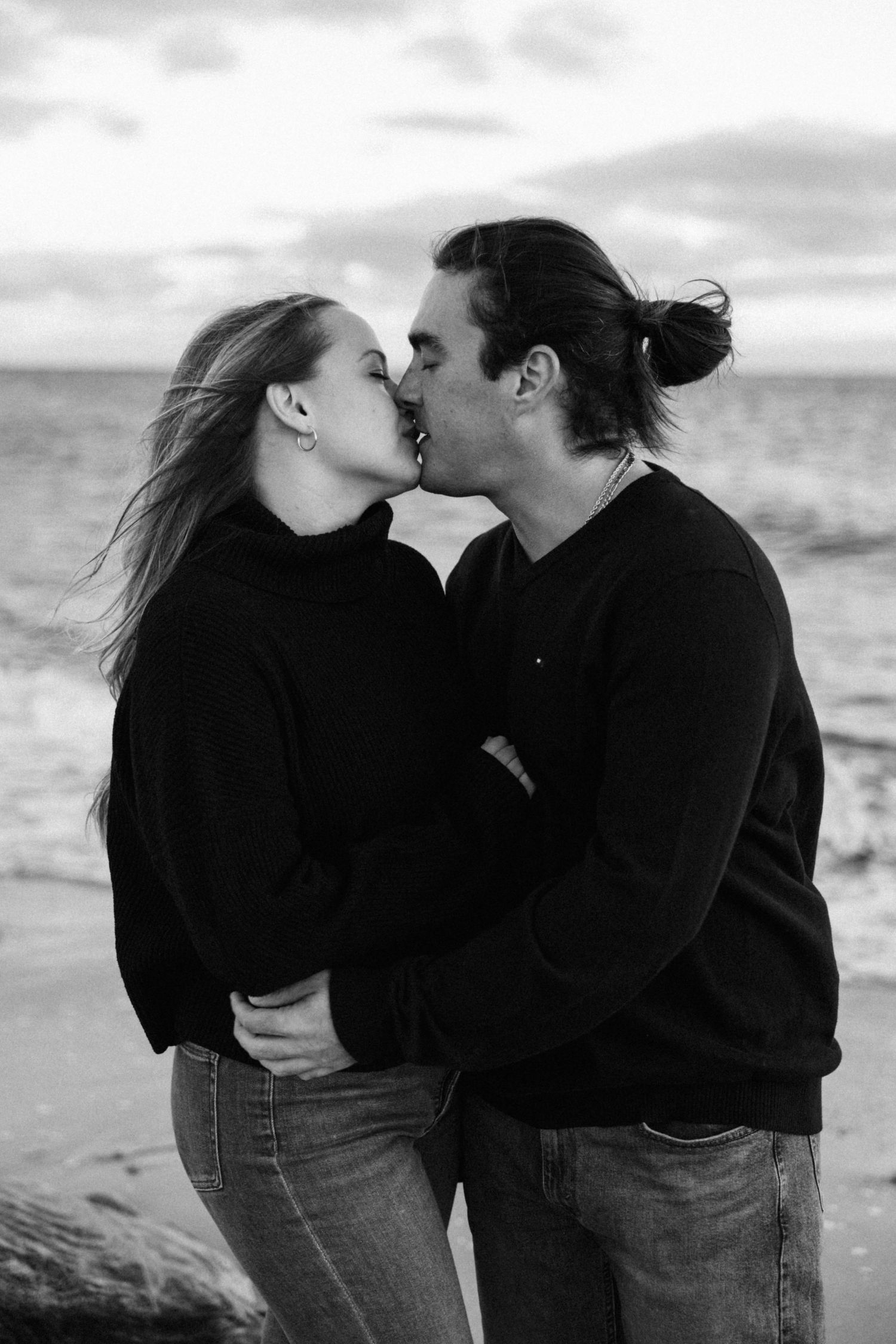 Black and white beach portraits of a couple in matching outfits sharing tender moments.