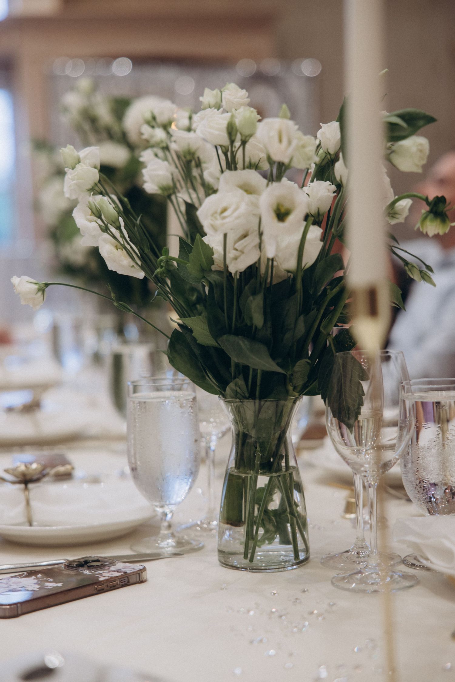 Elegant wedding table settings with white rose centerpieces in glass vases and crystal stemware.