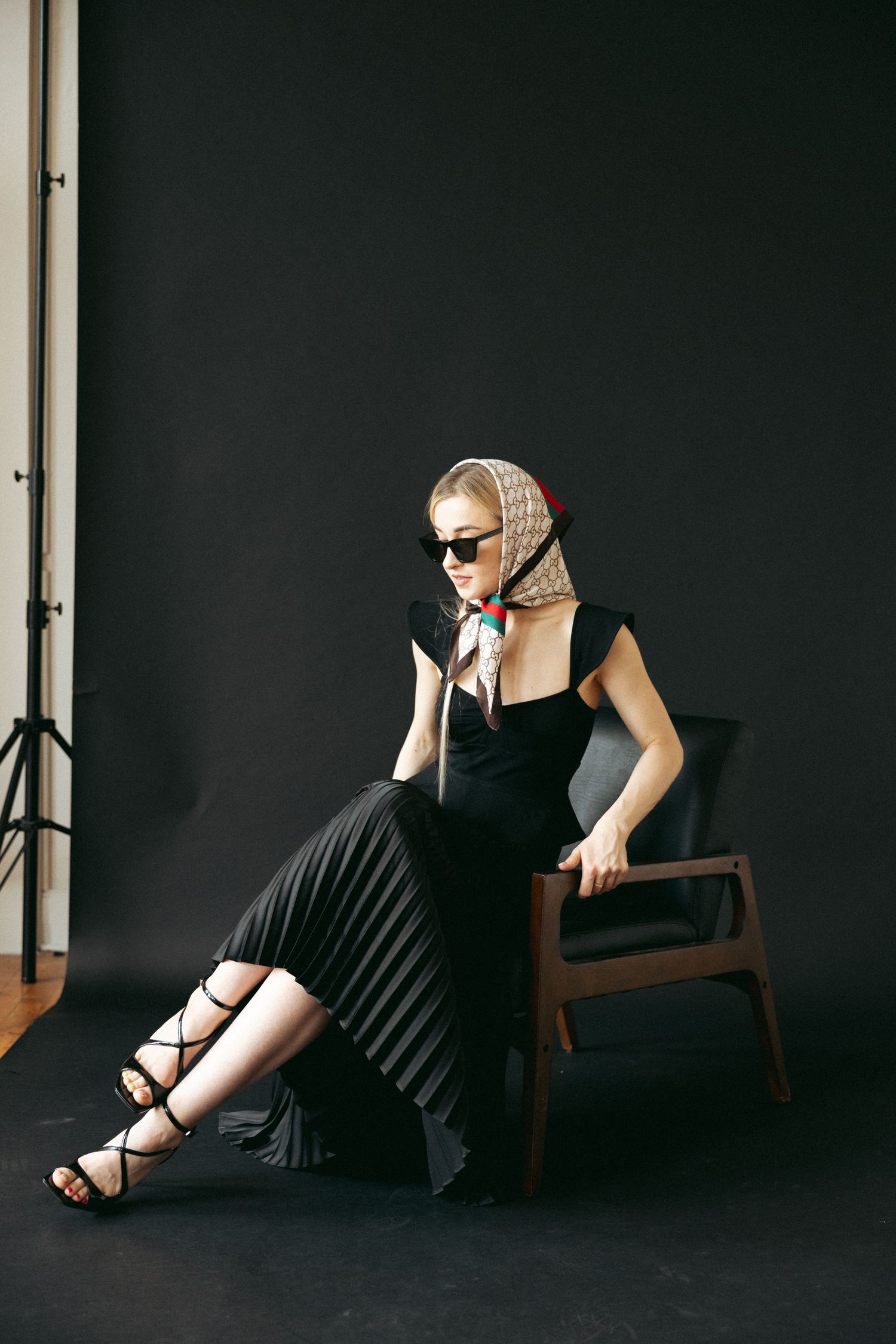Dark fashion series showing black dress and sunglasses against minimal studio backdrop.