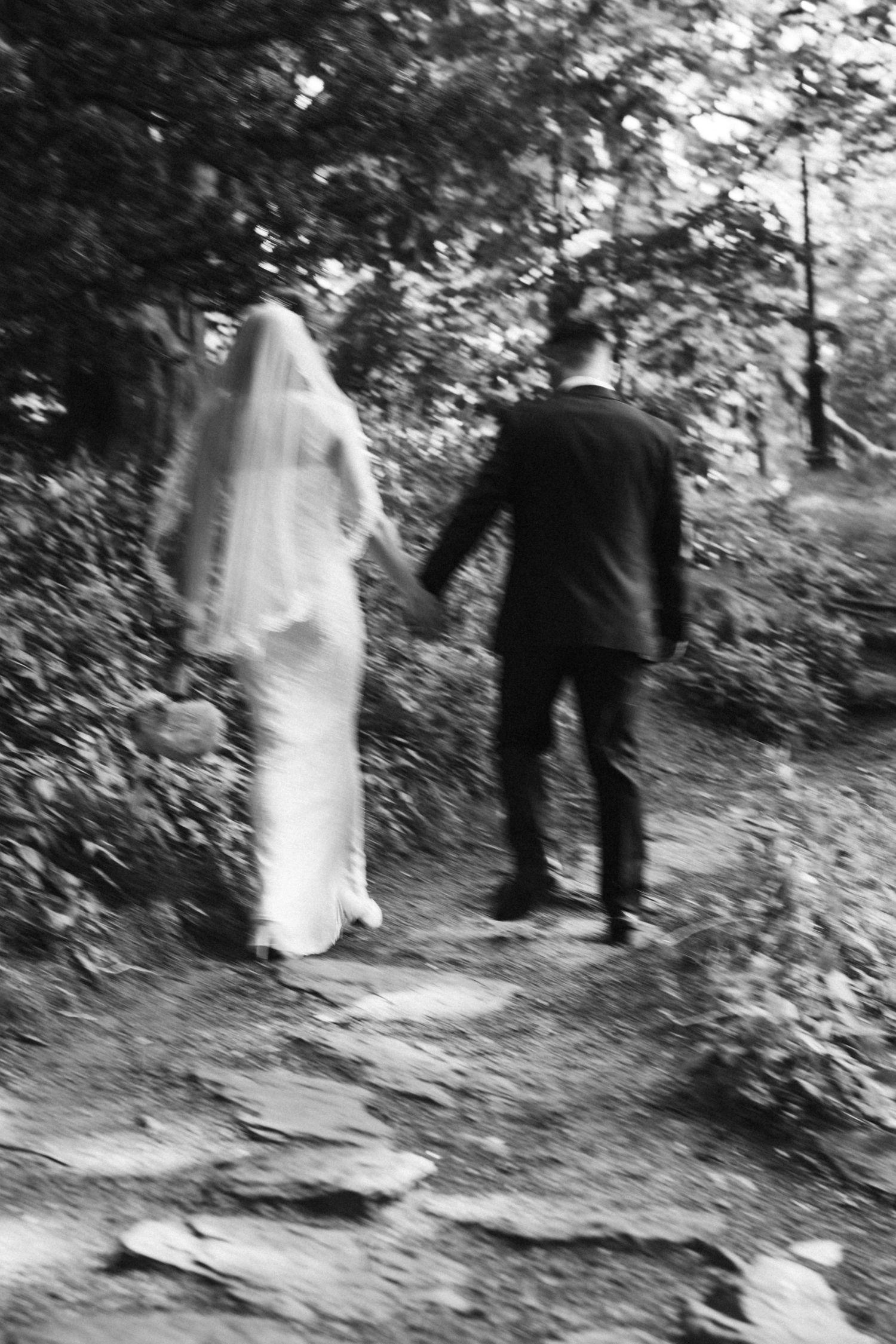 Black and white wedding photos showing a couple walking through a wooded path.