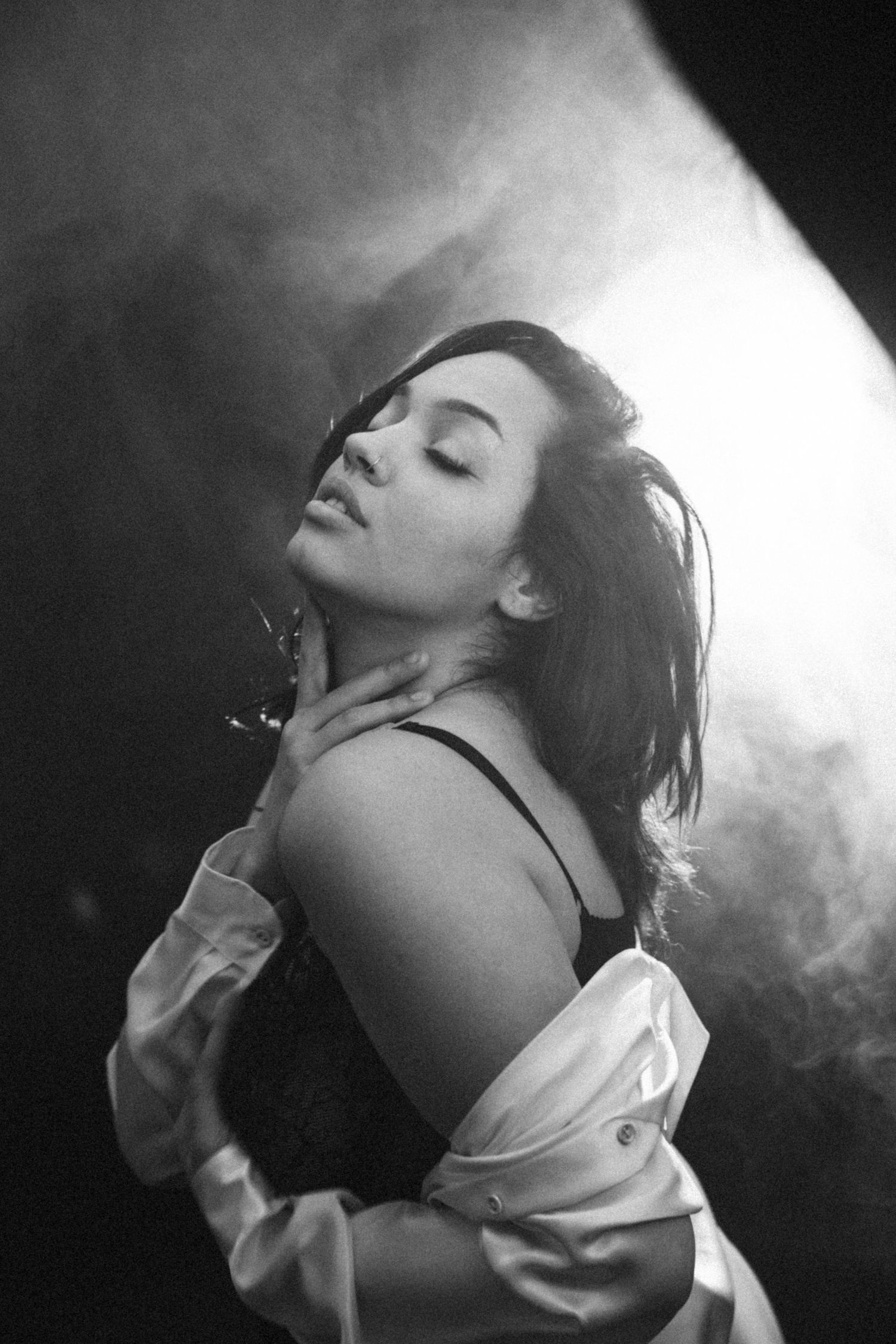 Dramatic black and white portrait with atmospheric lighting and white button-down shirt.