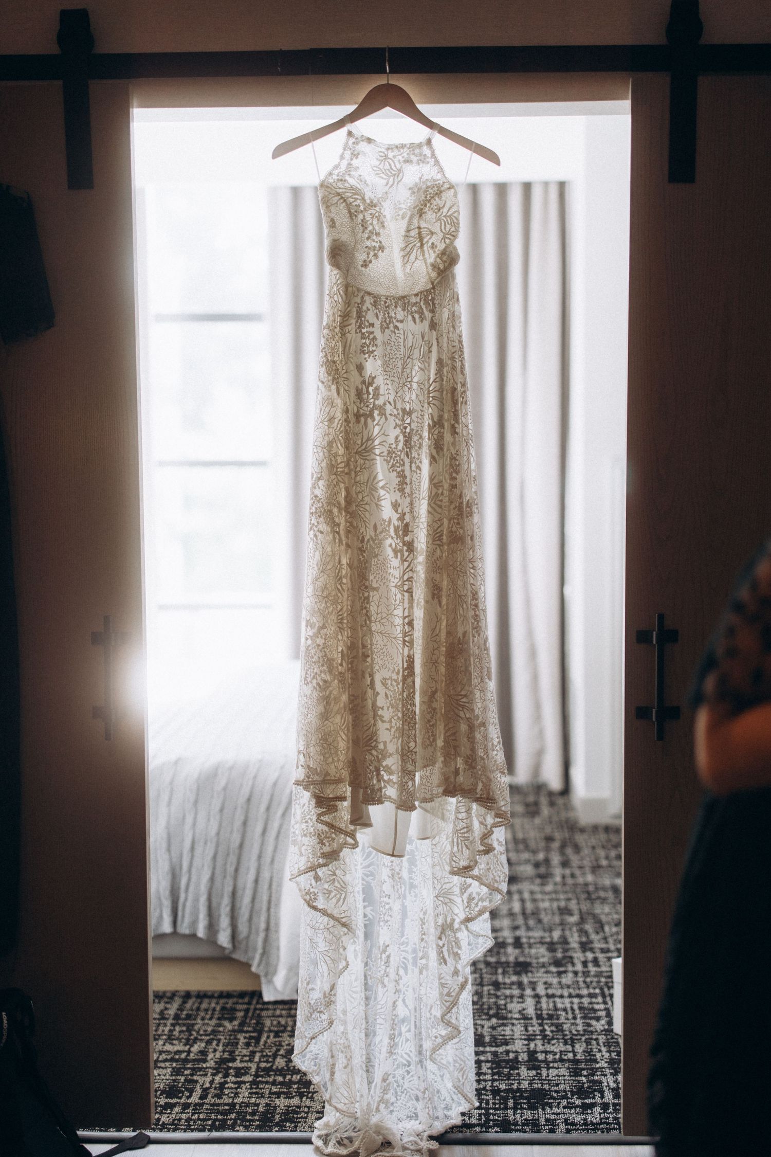 Elegant lace wedding dress hanging in window light.