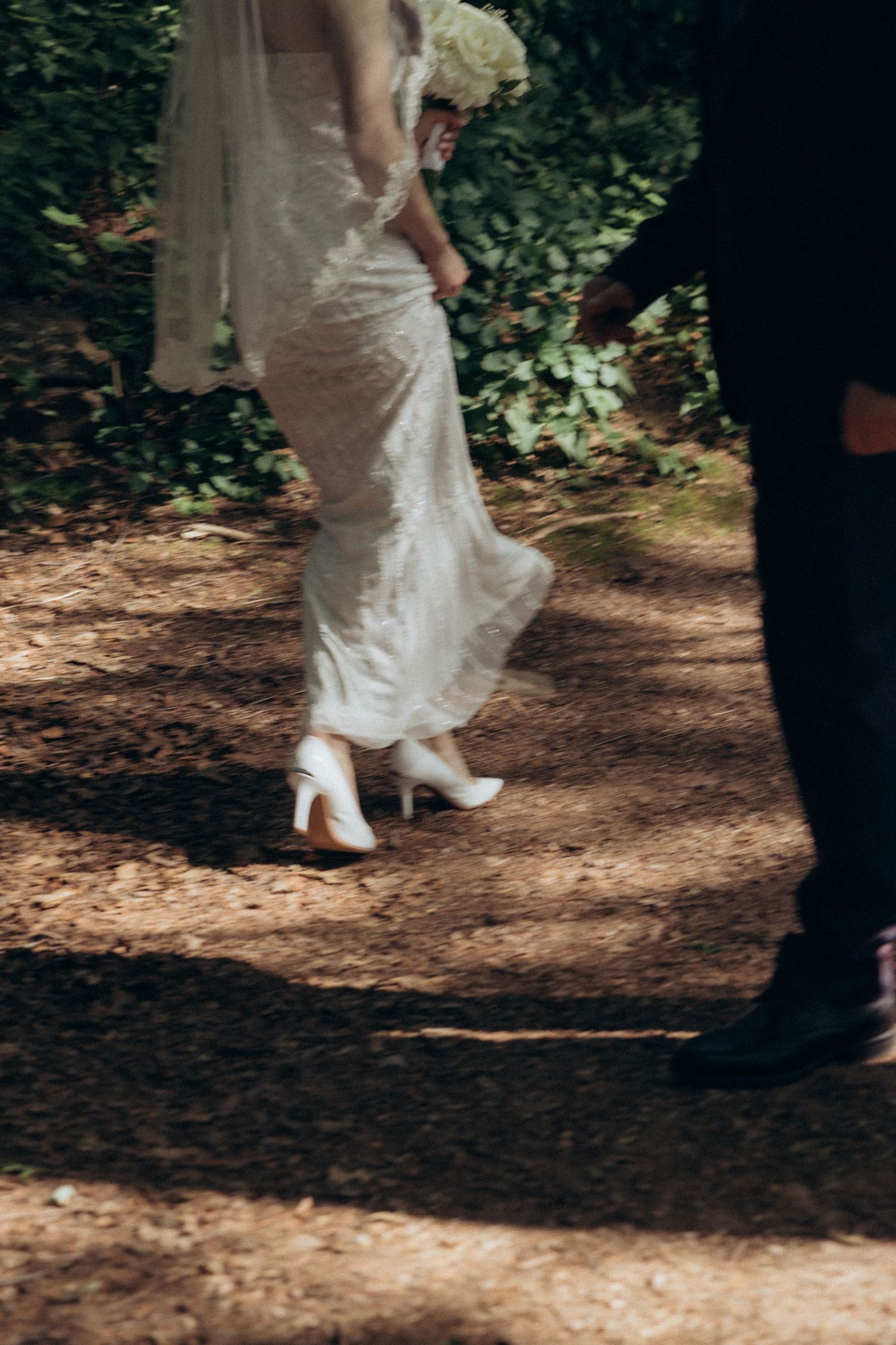 Close-up detail of wedding attire and footwear on a wooded path.