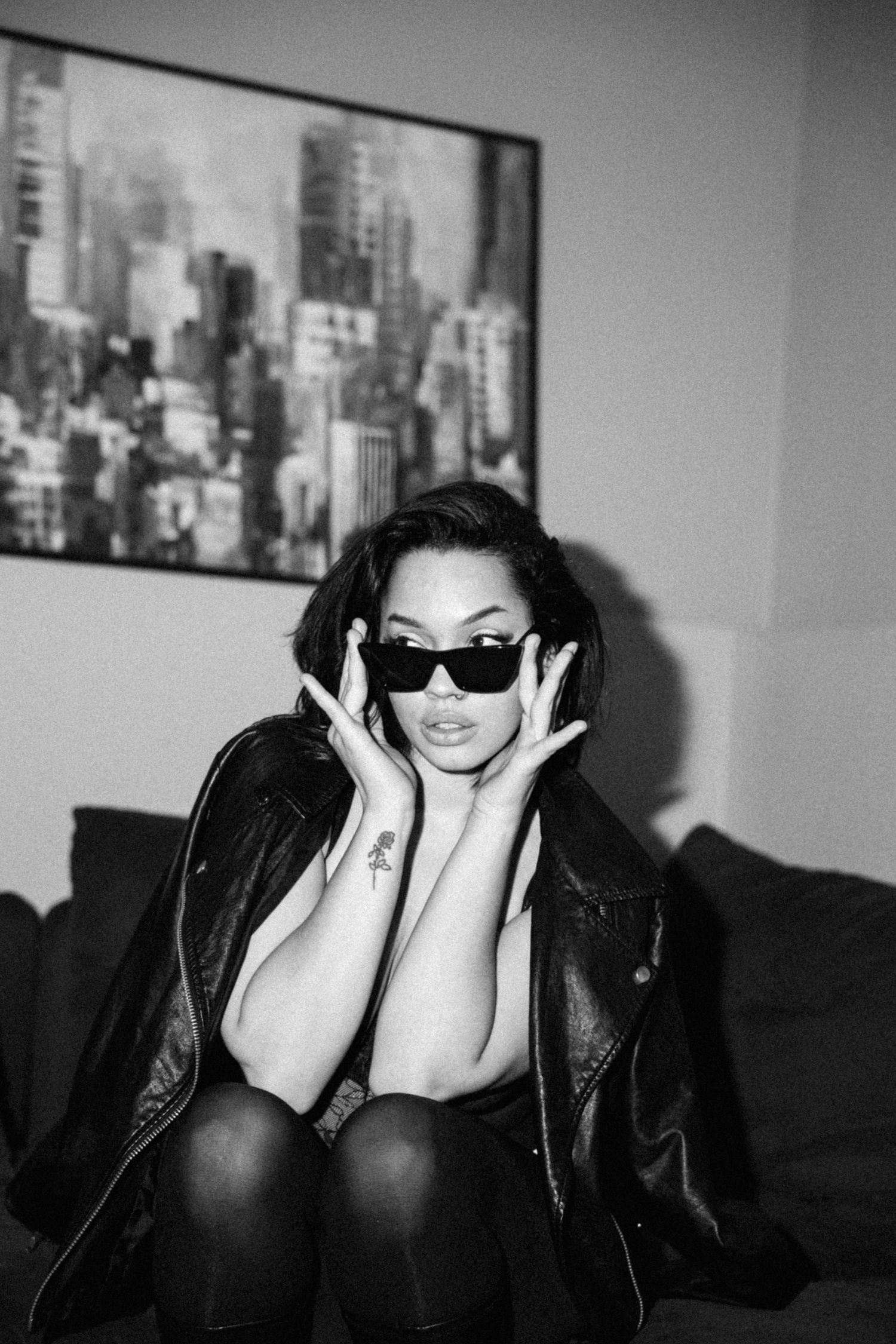 Dramatic black and white portrait with model in sunglasses against city skyline artwork.