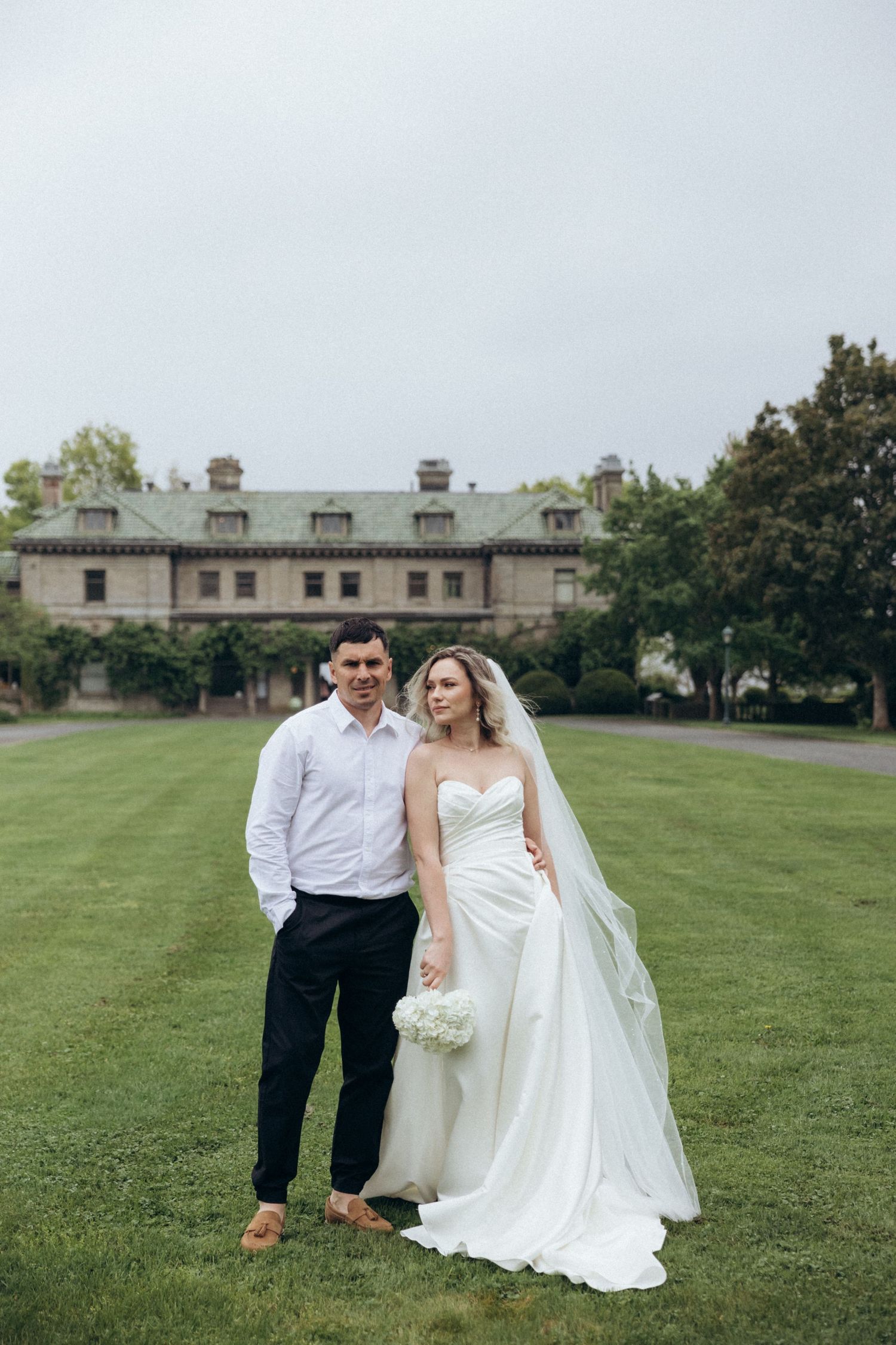 Wedding couple posing on expansive lawn of historic estate building.