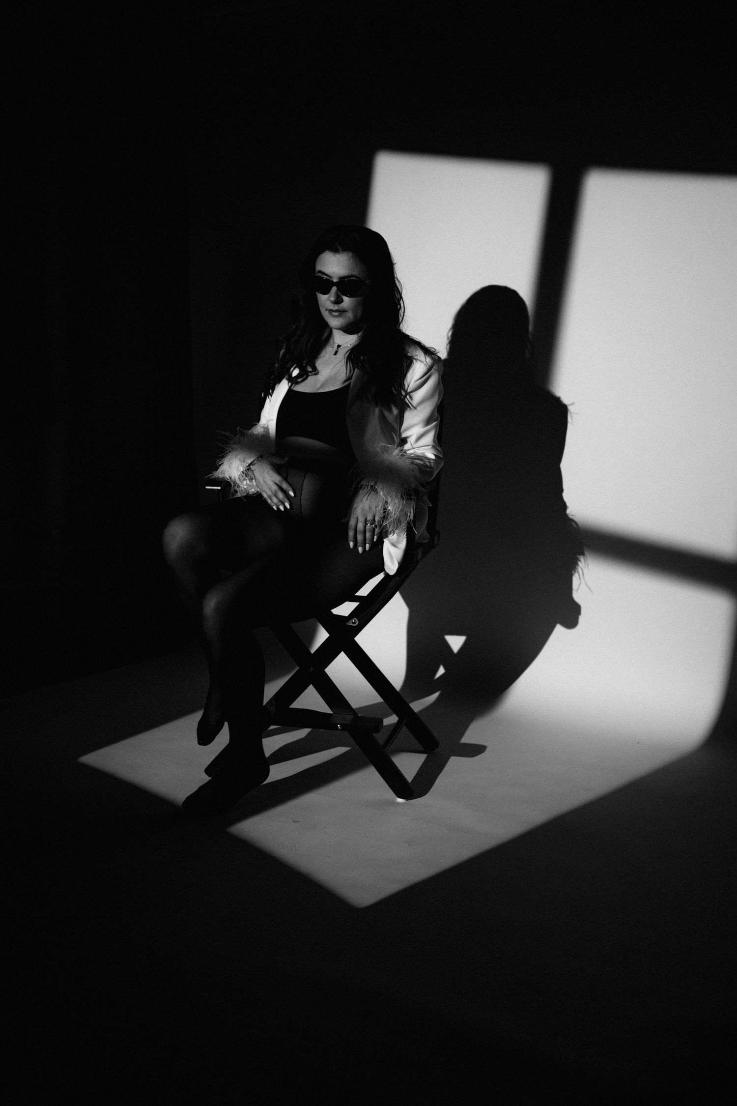 Dramatic noir-style portrait with strong shadow play from window light on seated figure.