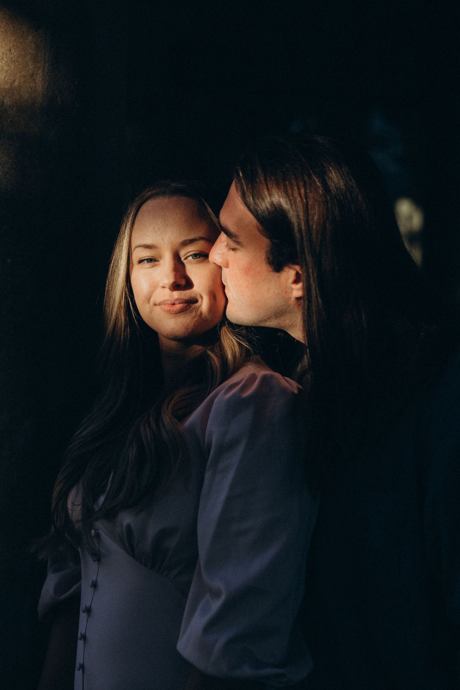 A moody portrait of a couple in dark clothing with dramatic side lighting.