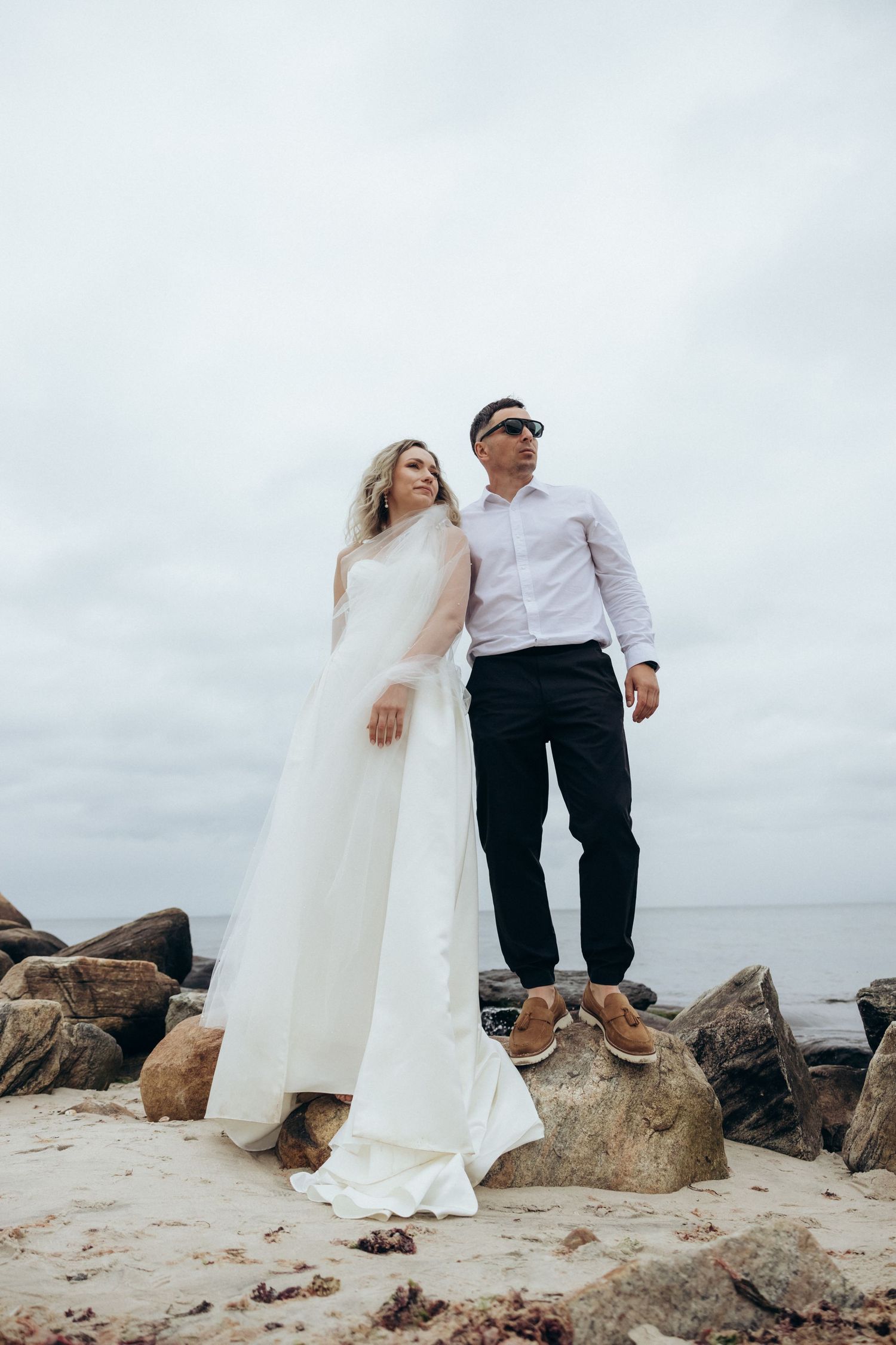 Wedding couple poses creatively on rocky beach terrain in formal attire creating artistic sequences.
