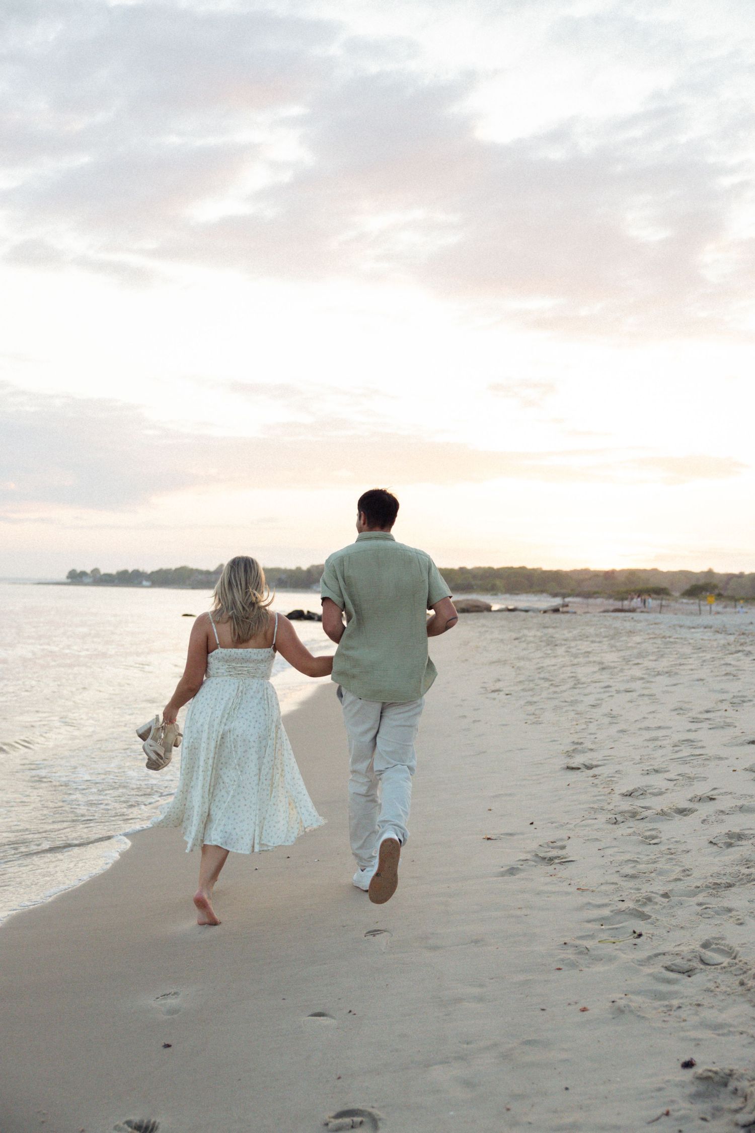 A couple running playfully together on a sandy beach during sunset.