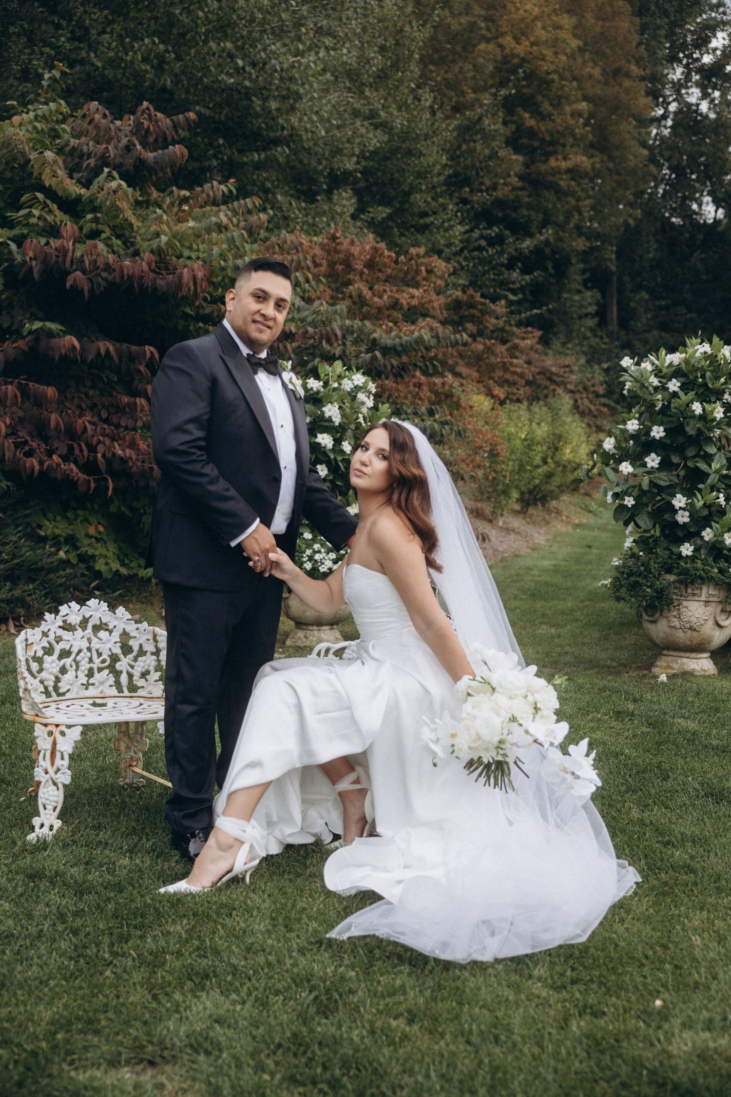 Newlyweds share a romantic moment on a manicured lawn with white floral decorations.