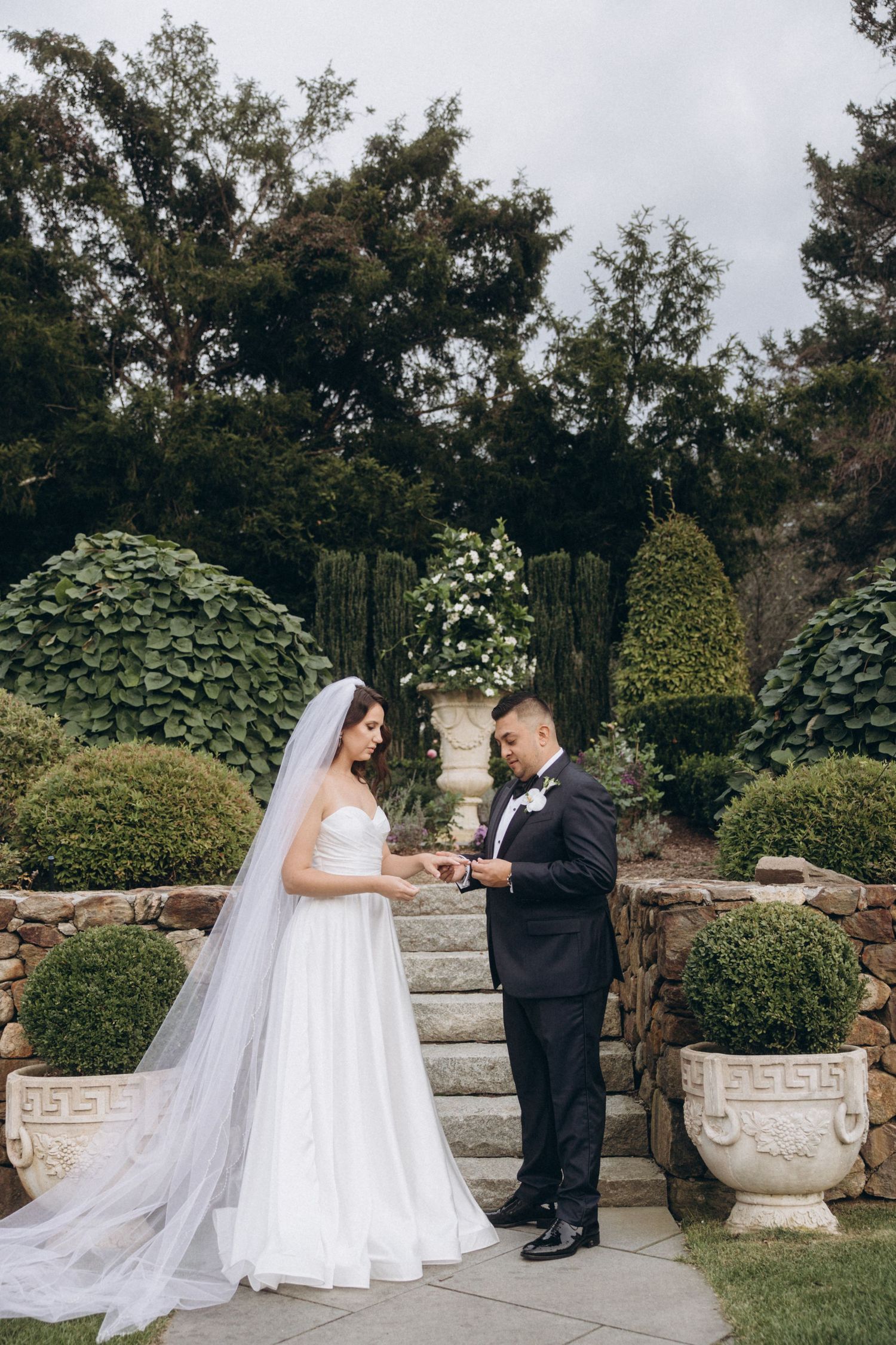 Classic wedding couple standing on a stone patio surrounded by lush garden landscaping.