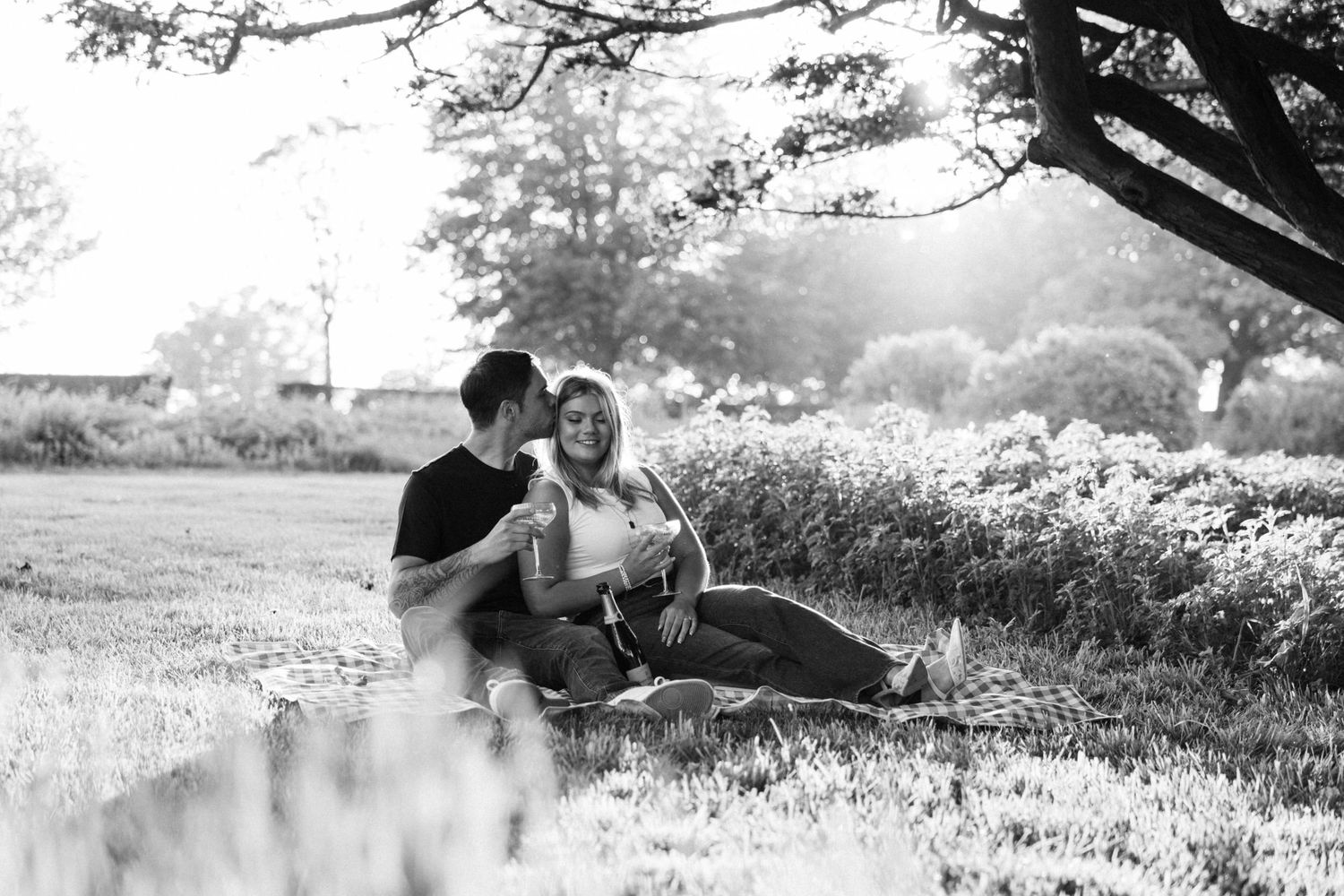 Two people share drinks while relaxing under a tree on a bright day.