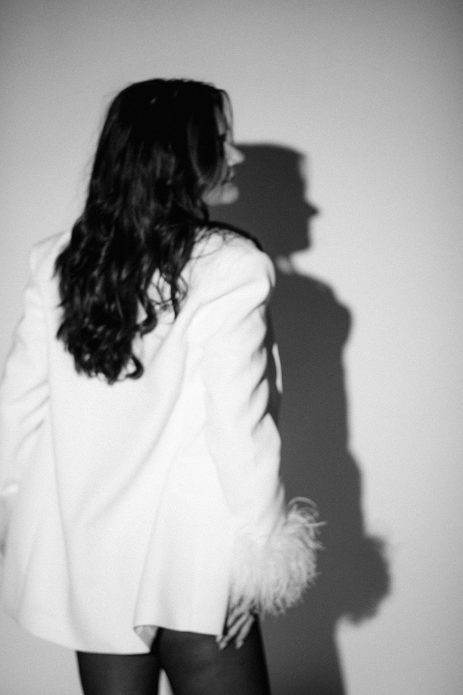 Artistic profile shot with dramatic shadow cast on wall from white blazer.