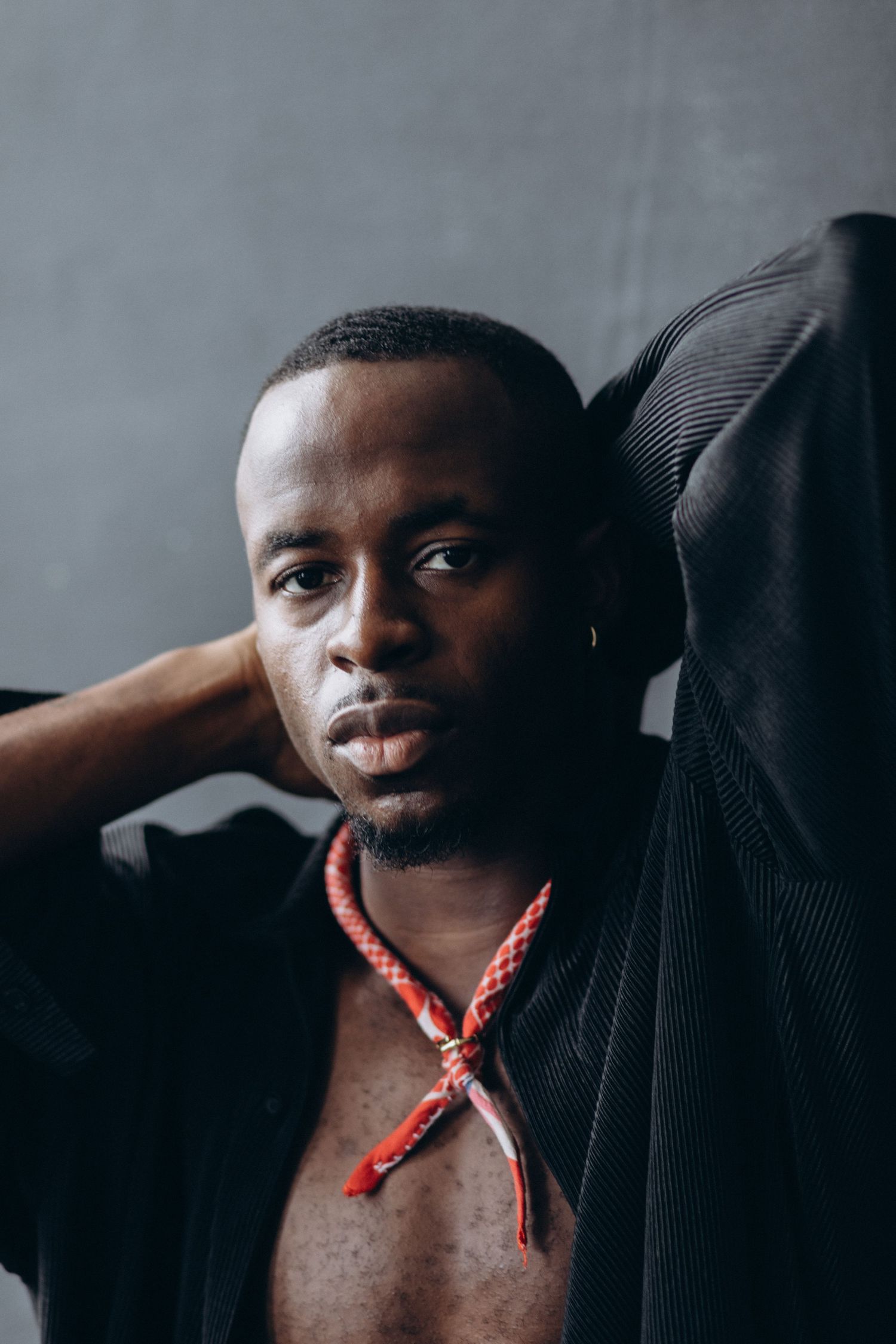Artistic portrait series with subject wearing a black sweater and red necklace against grey background.