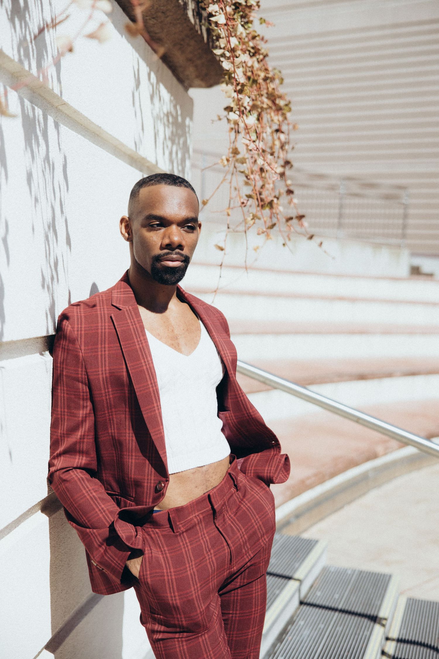 A dynamic fashion photo series featuring a burgundy checkered suit against a light architectural background.