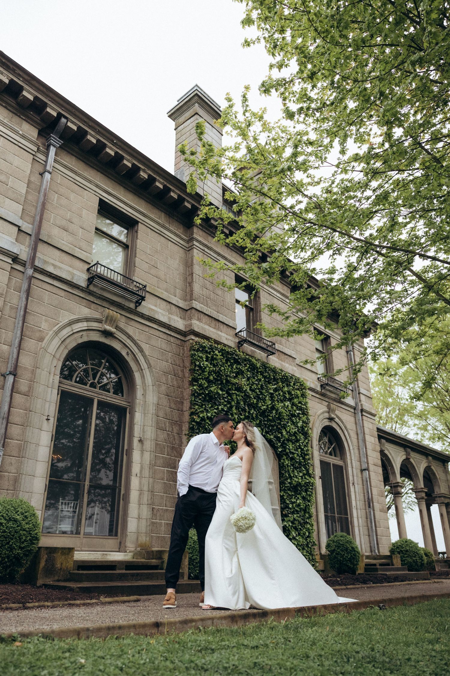 Wedding photos taken against a historic stone building with ivy and arched windows.