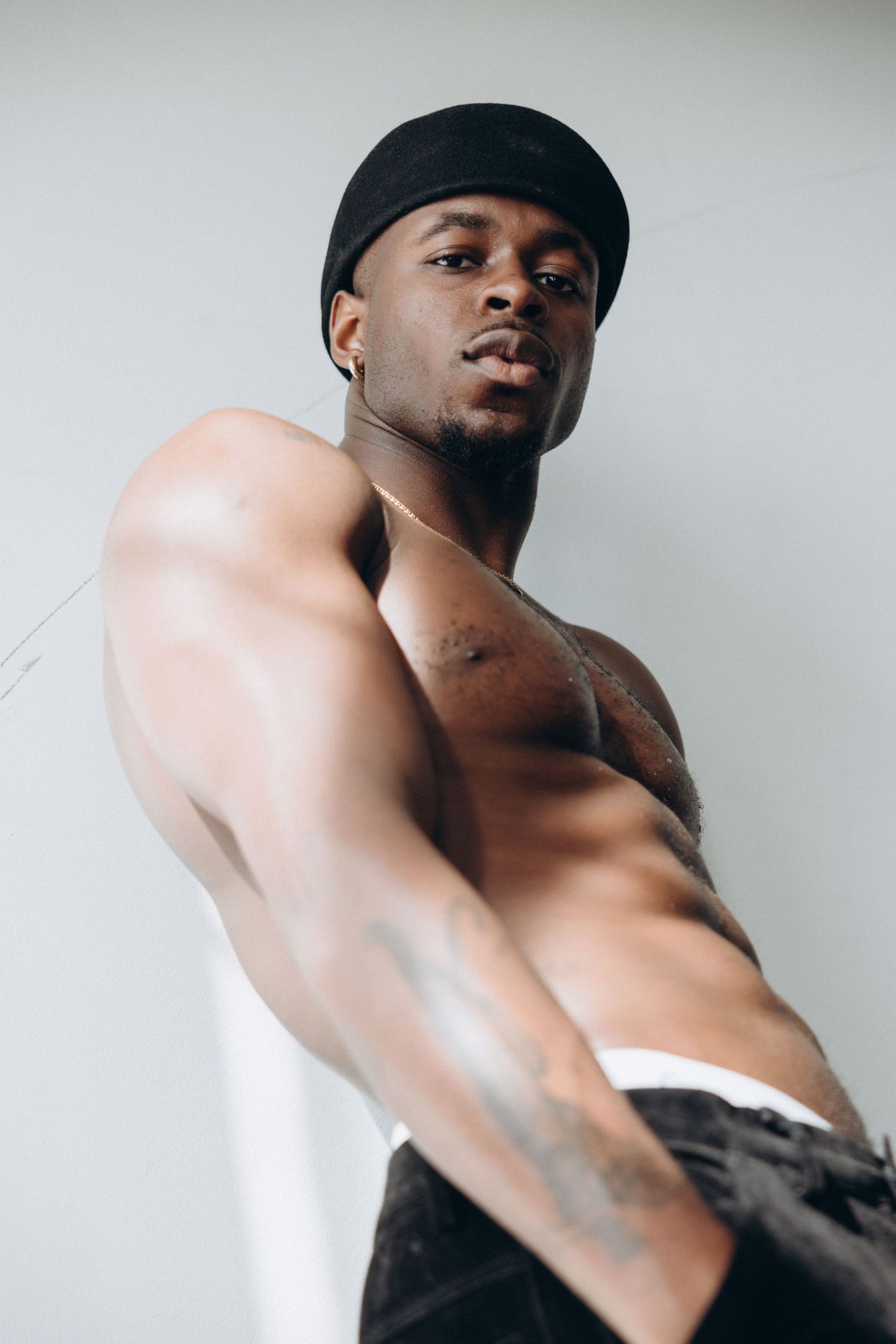 Shirtless athletic model wearing a black beanie poses against white background in dramatic lighting.