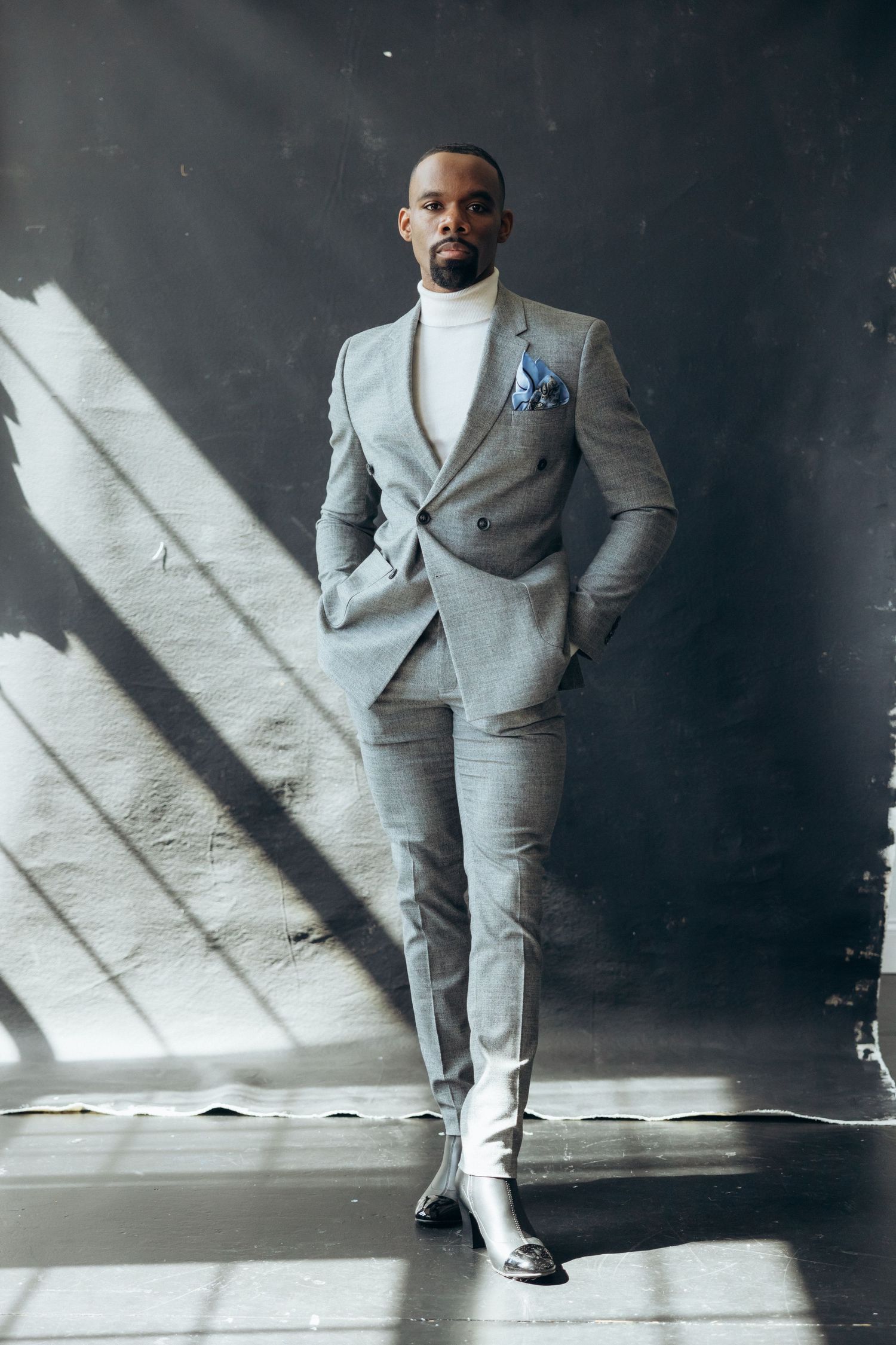 Stylish grey suit with white turtleneck and pocket square in dramatic lighting.